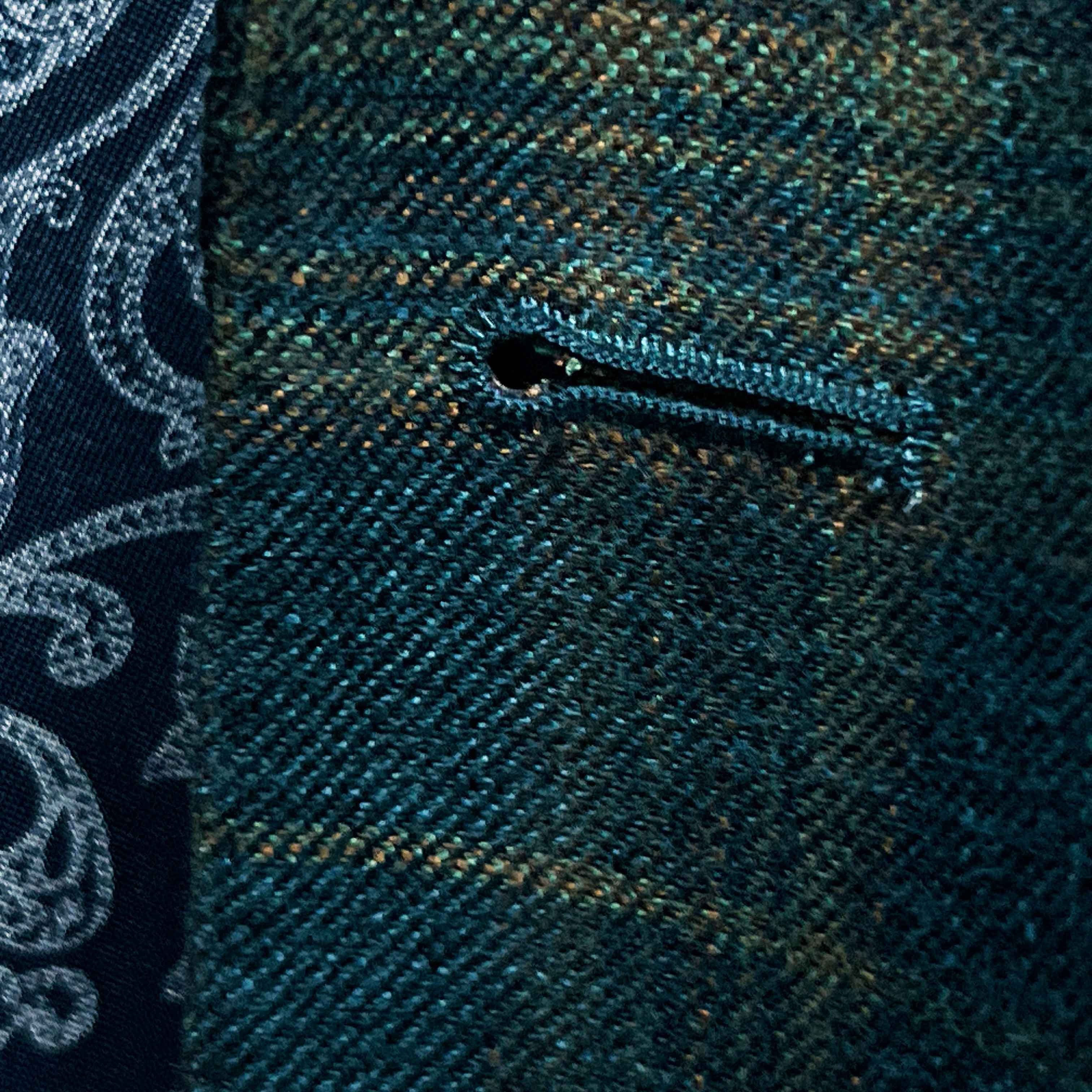 Detailed macro shot of hand-finished buttonhole stitching on deep teal green multi check suit with olive green contrast thread
