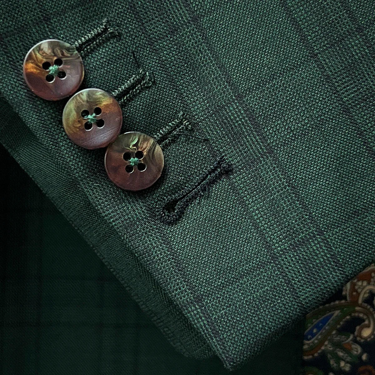 Sport coat jacket sleeve cuff showing functional buttonholes with contrast black accent stitching on hunter green checkered fabric