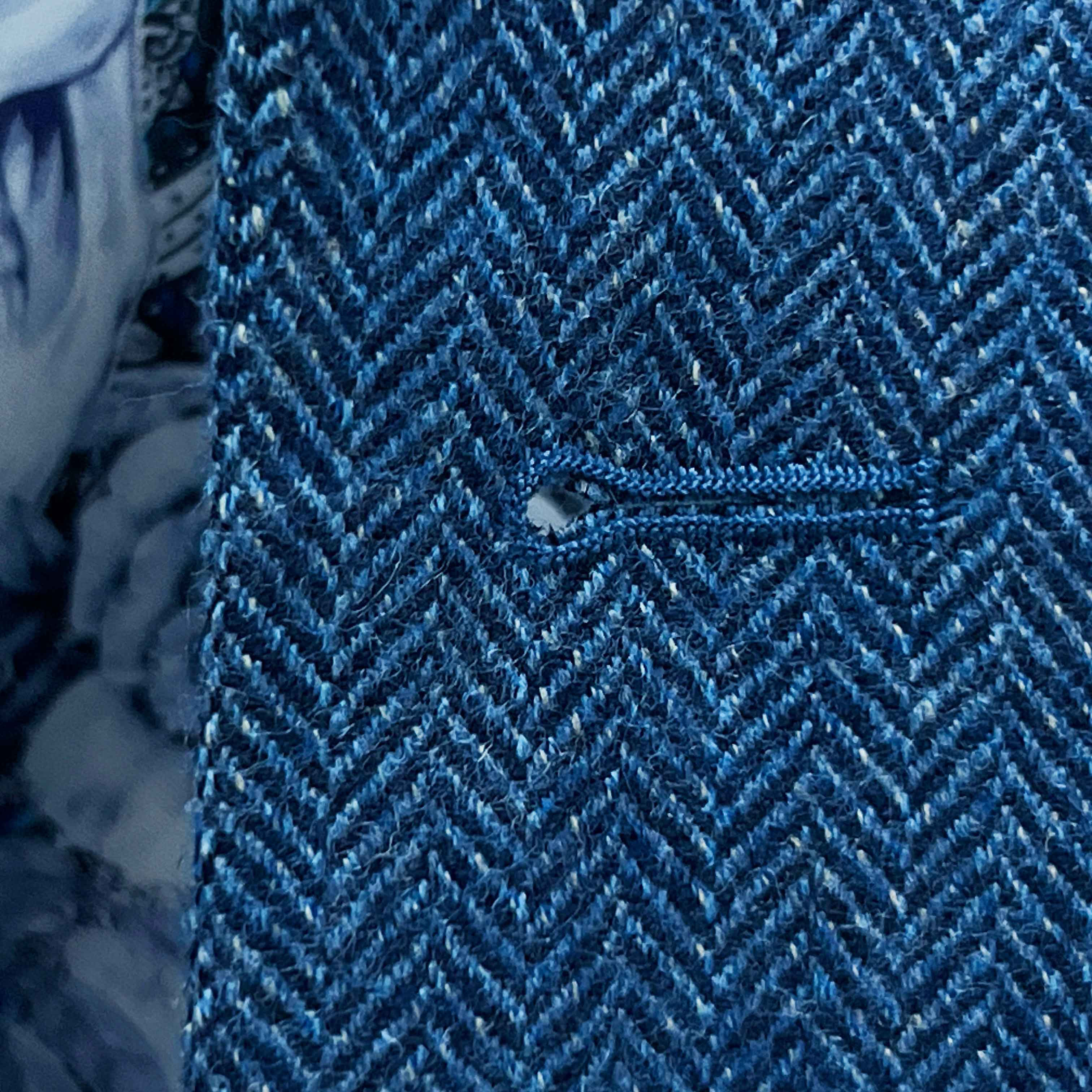Detailed macro shot of hand-finished buttonhole stitching on indigo blue herringbone tweed sport coat with royal blue contrast thread