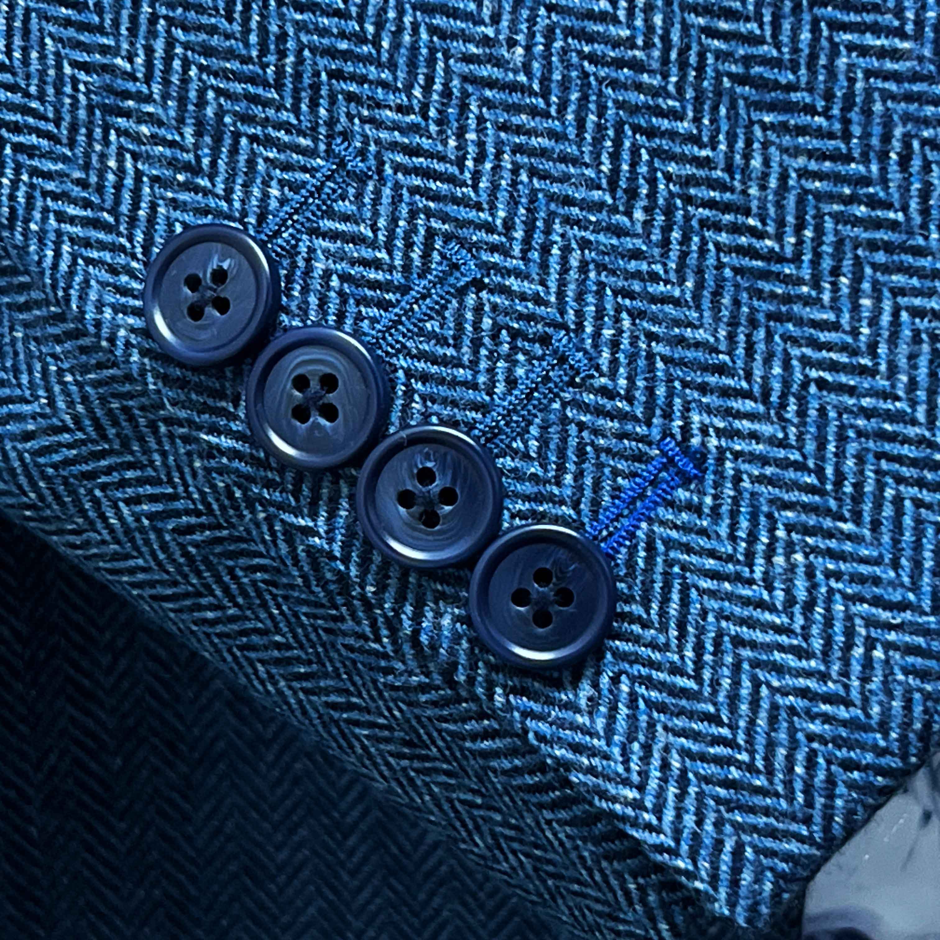 Sport coat sleeve cuff showing functional buttonholes with contrast royal blue accent stitching on indigo blue herringbone tweed fabric