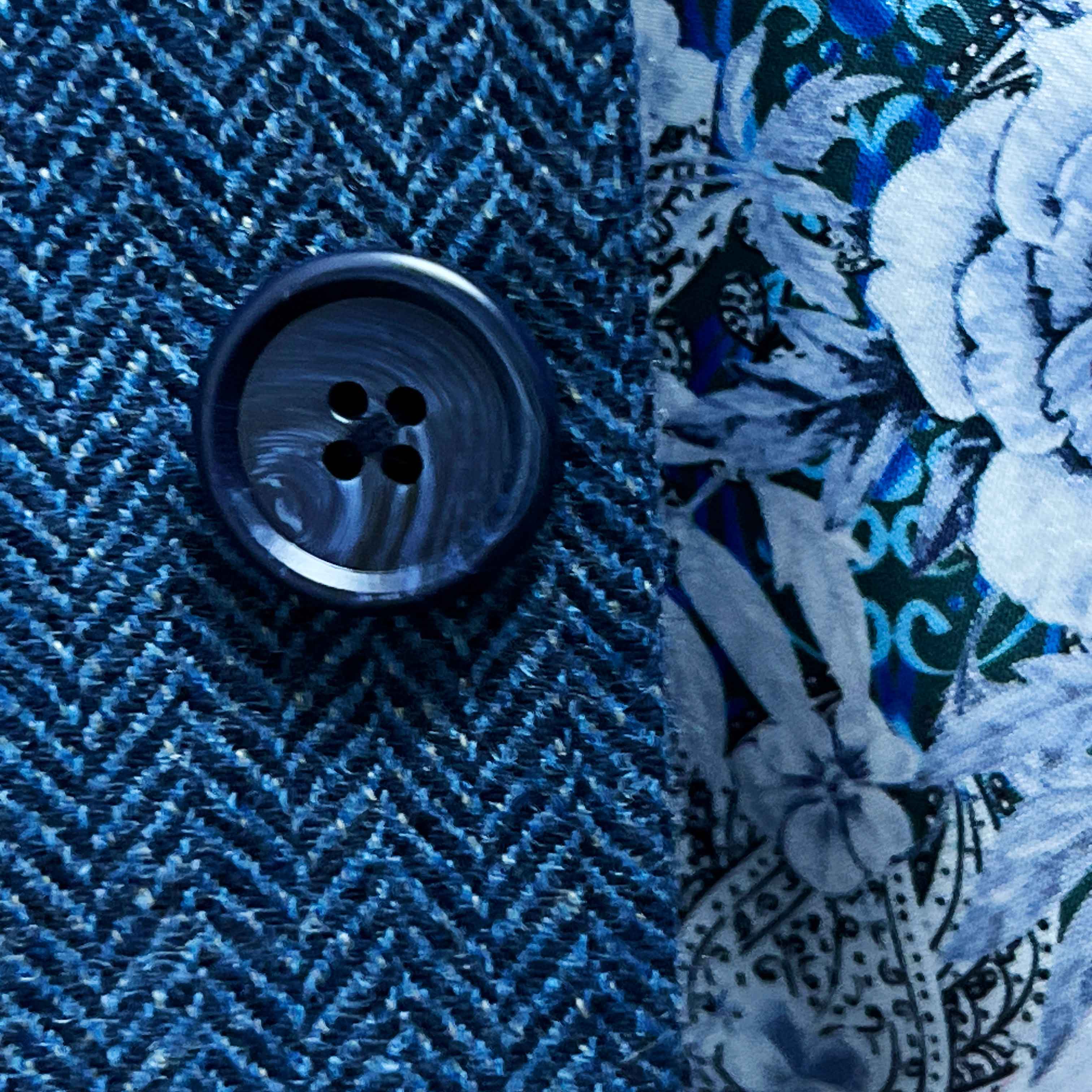 Close-up of a blue textured fabric with a button and floral embroidery.