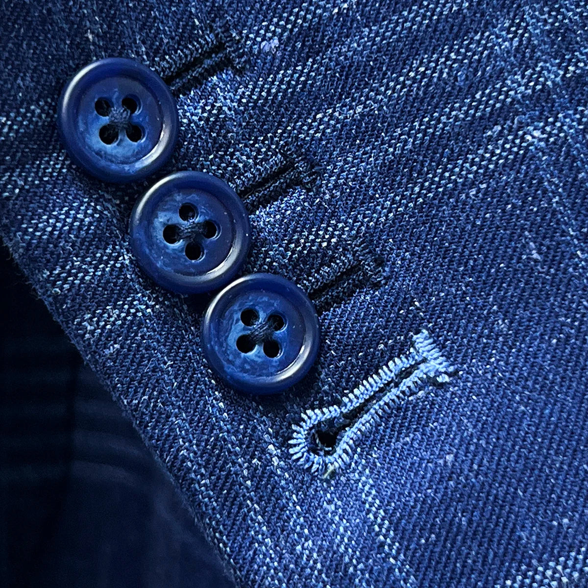 Close-up of functional sleeve buttonholes with white contrast stitching, demonstrating authentic custom tailoring on working sleeve buttons