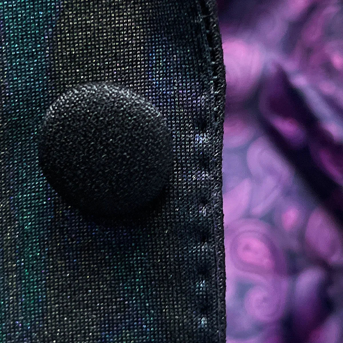 Macro detail of iridescent teal green purple black tuxedo fabric showing abstract pattern and colour-shifting properties under lighting