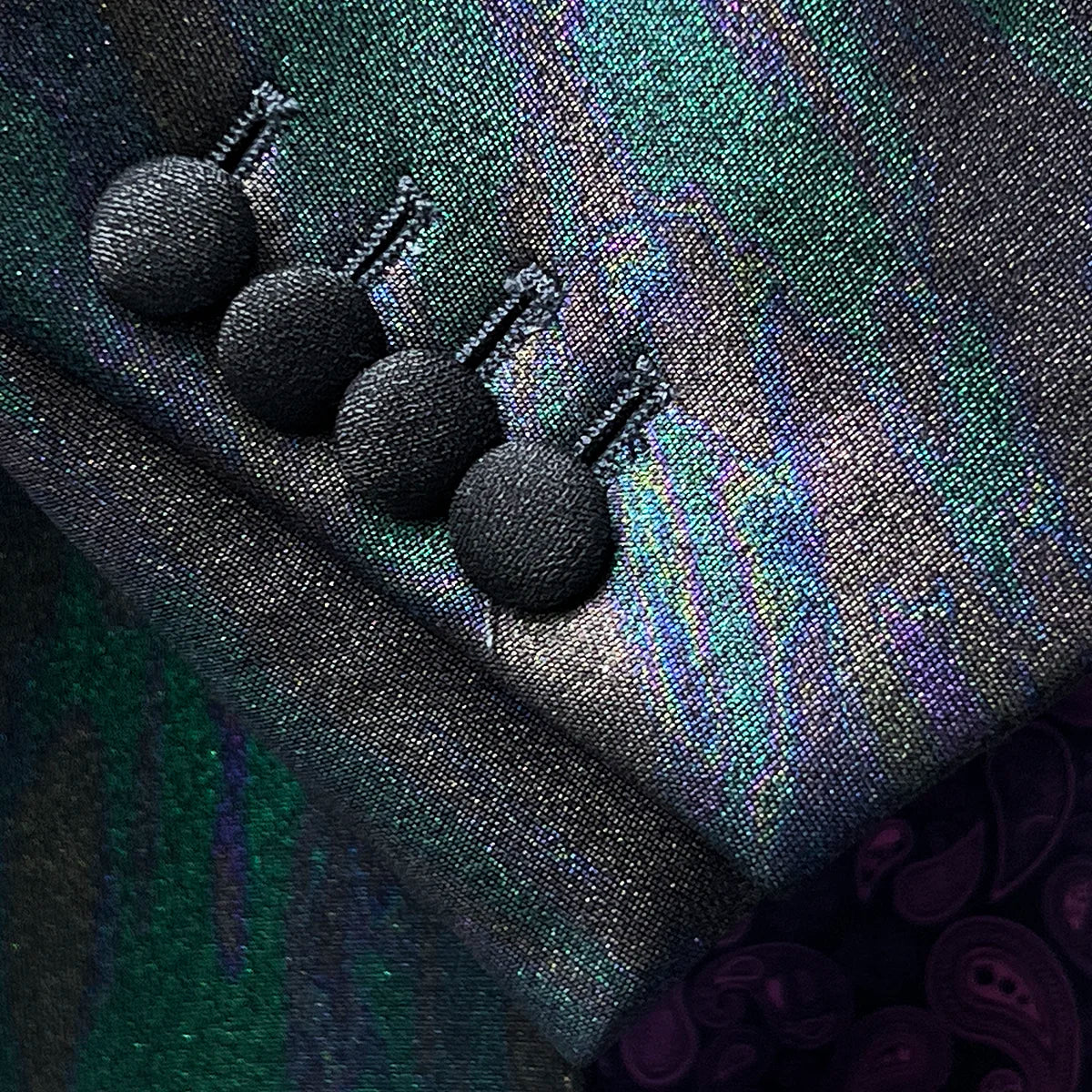 Tuxedo jacket sleeve cuff showing functional buttonholes with black fabric-covered buttons on iridescent colour-shifting fabric