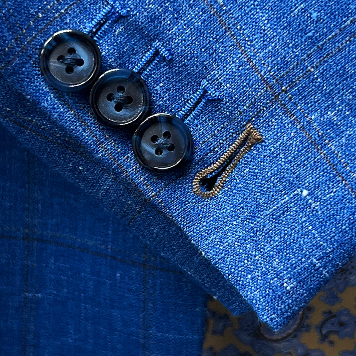 Working sleeve buttonholes with chocolate brown contrast stitching demonstrating authentic custom tailoring detail