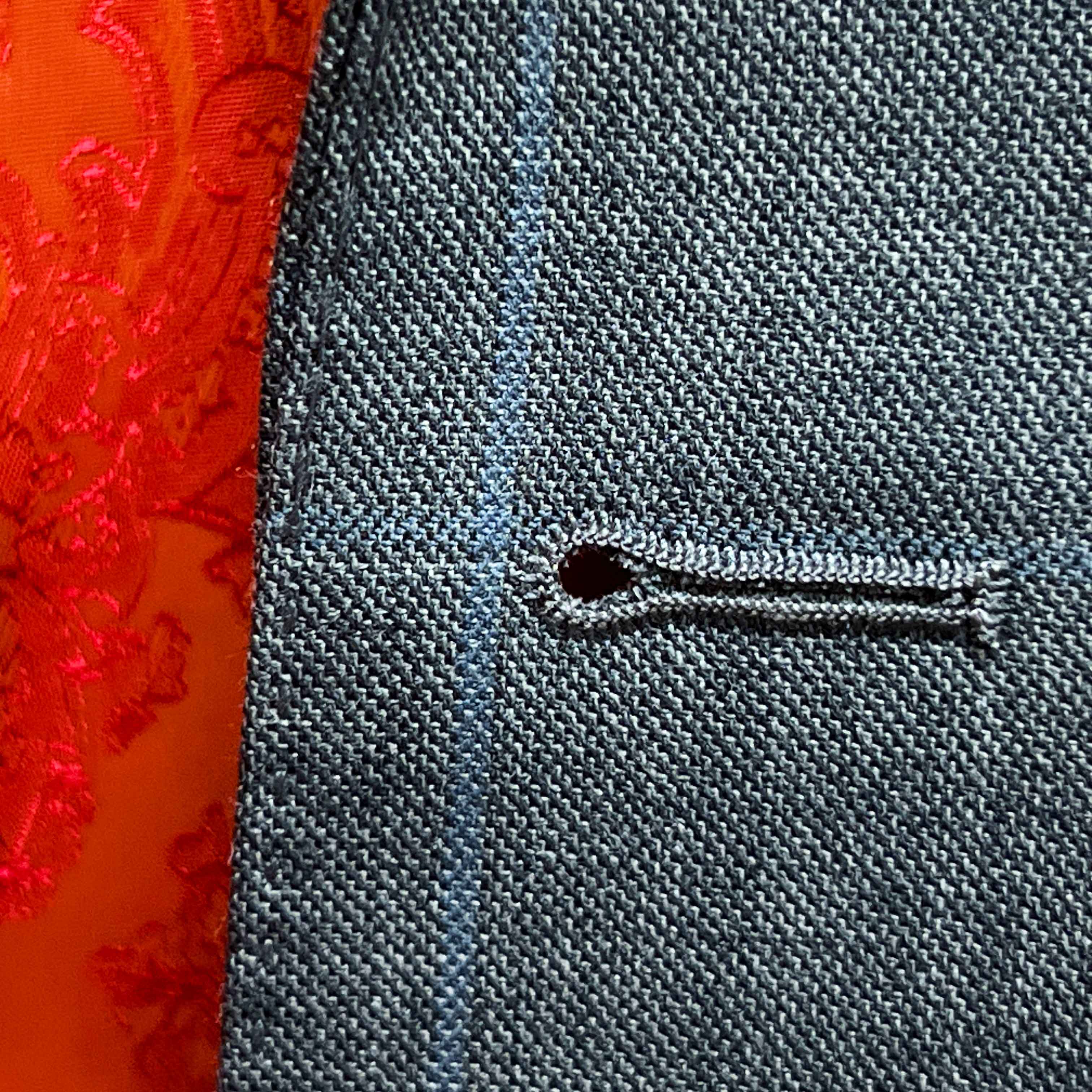 Detailed macro shot of hand-finished buttonhole stitching on light gray with light blue windowpane sport coat with bright orange contrast thread