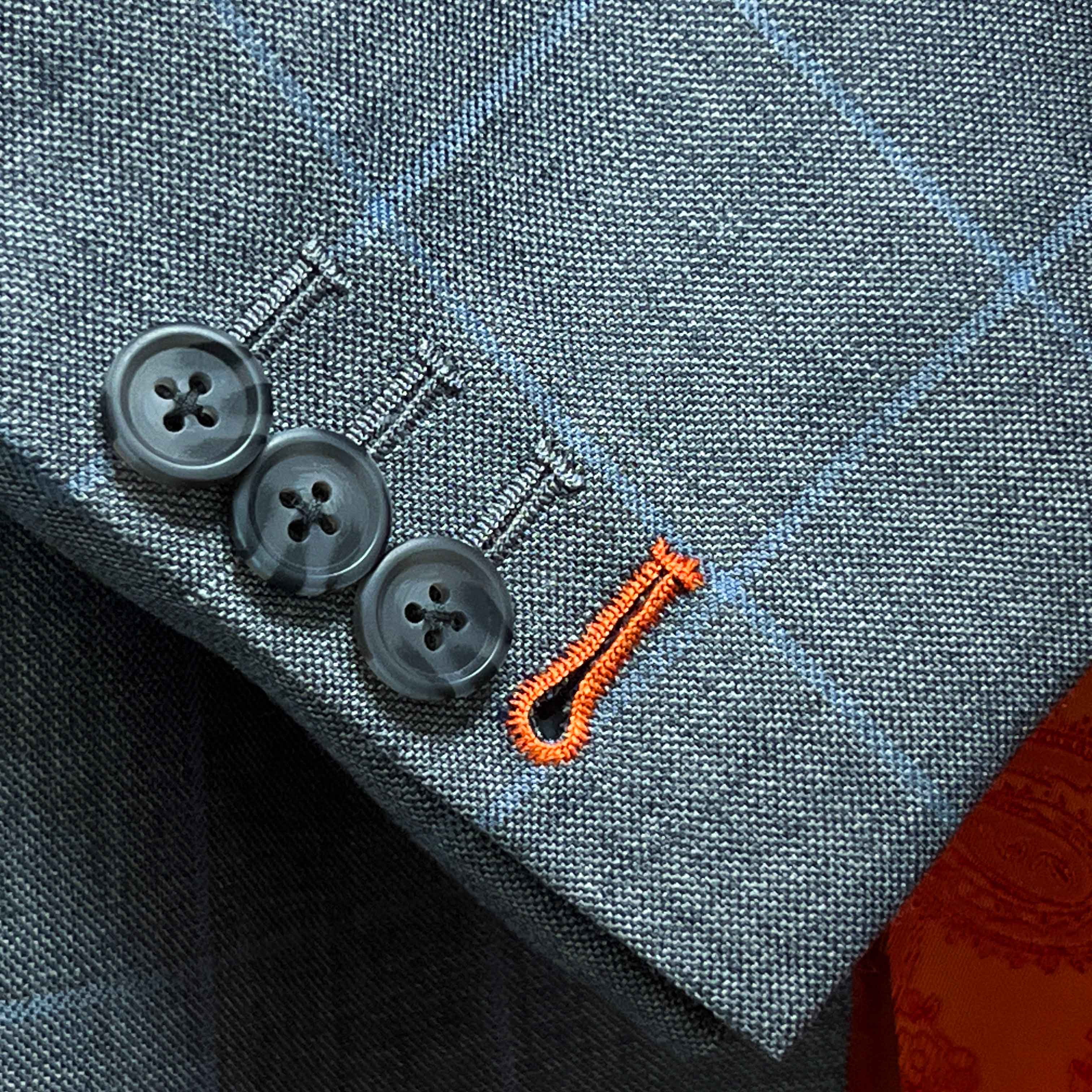 Contrast bright orange accent buttonholes on light gray with light blue windowpane sport coat sleeve showing precise hand-finished stitching