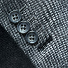 Close-up of working sleeve buttons with black contrast buttonholes and pick stitching on light grey tweed