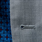 Macro view of buttonhole stitching on light grey sharkskin suit, highlighting fabric quality