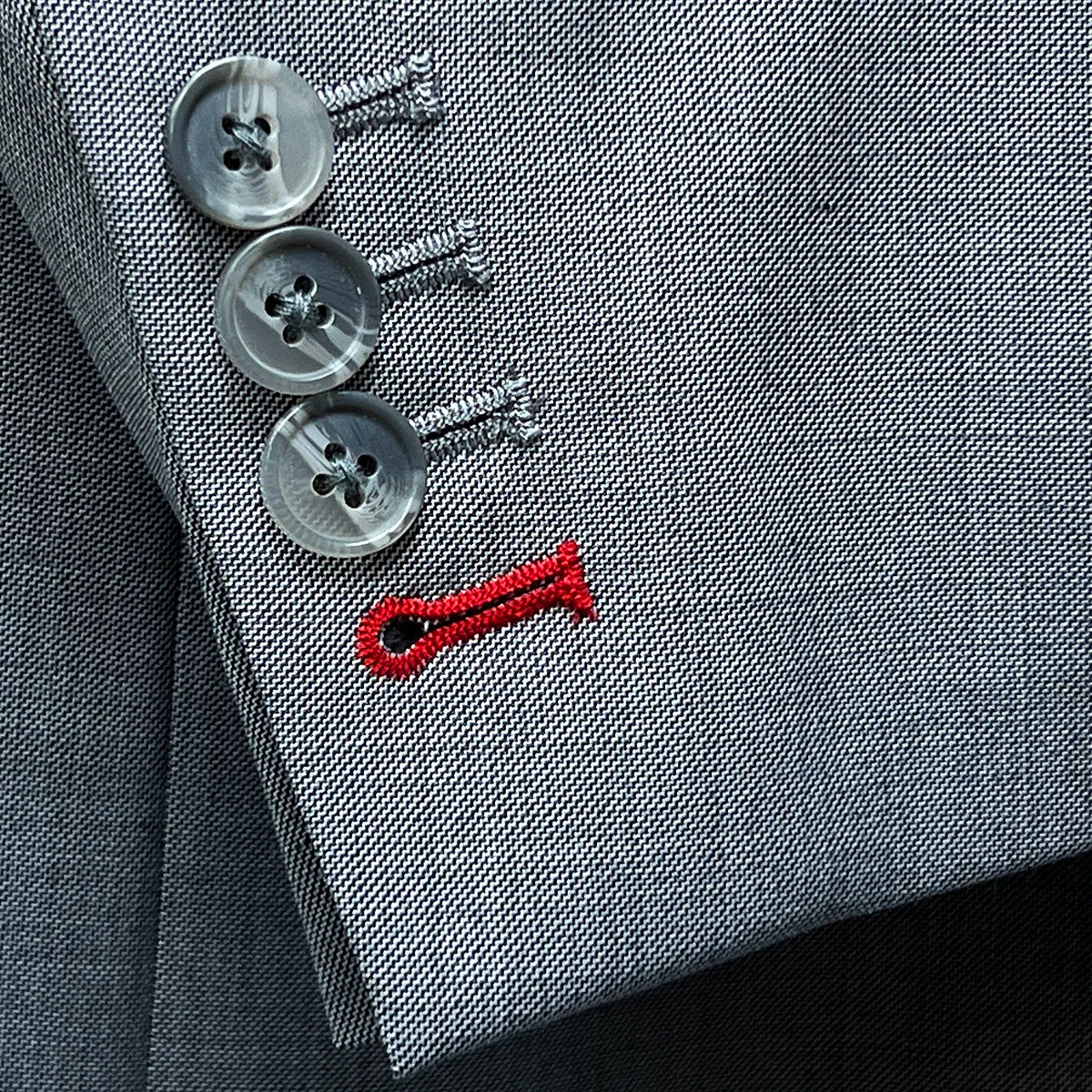 Detail shot of suit jacket sleeve showing functional buttonholes with light grey horn buttons