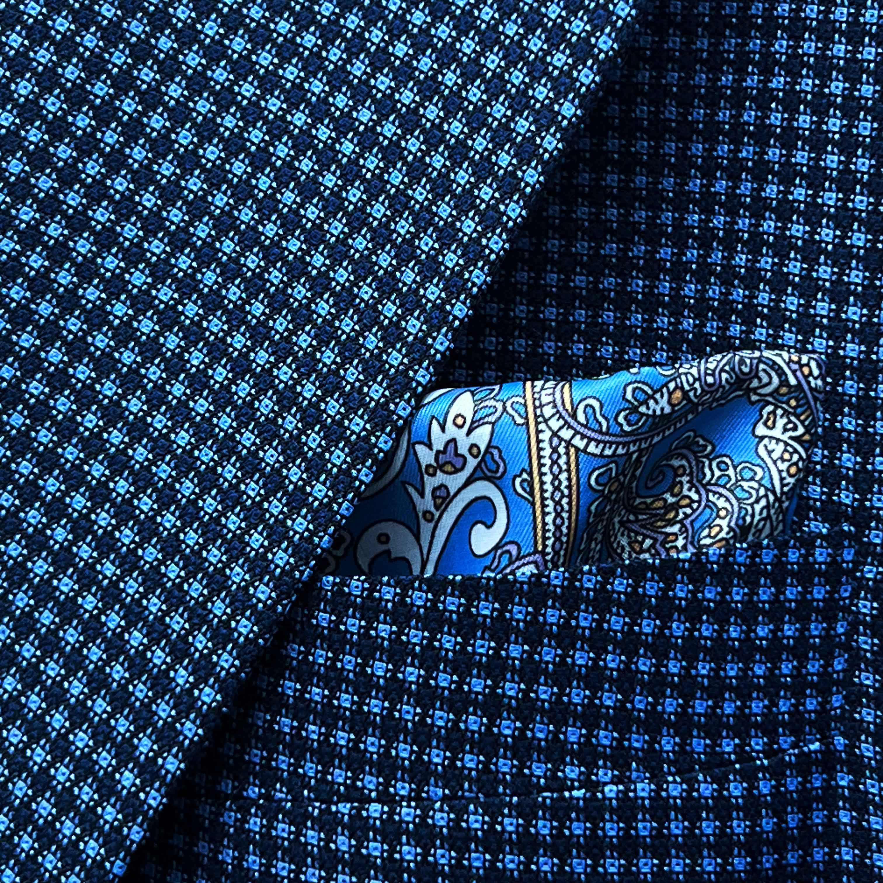 Breast pocket of medium blue micro check sport coat with matching paisley pocket square and hand-finished edges