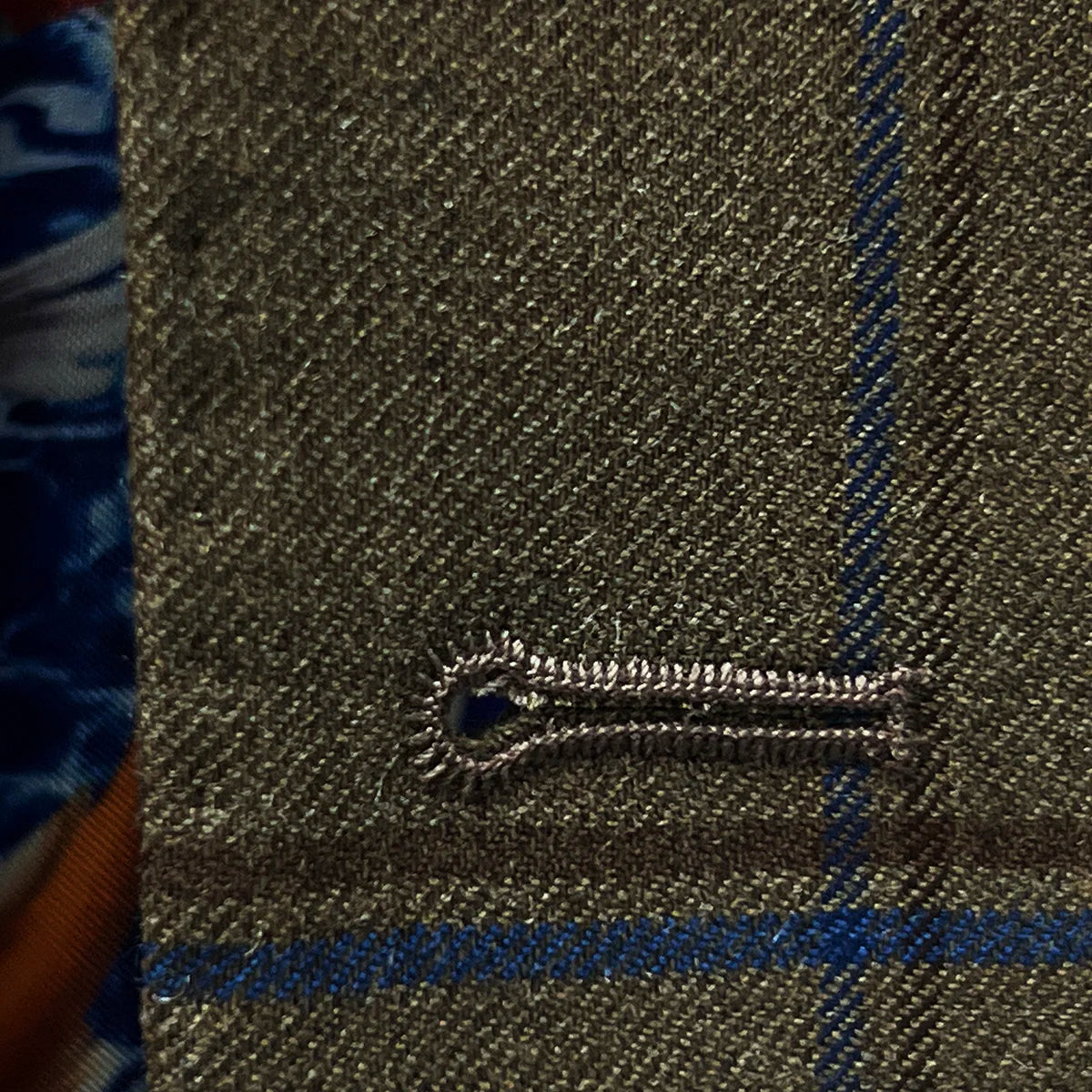 Macro view of blue contrast buttonhole stitching on medium brown windowpane fabric