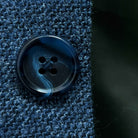 Close-up of dark navy horn buttons with light blue marbling on medium steel blue hopsack sport coat showing natural patterns