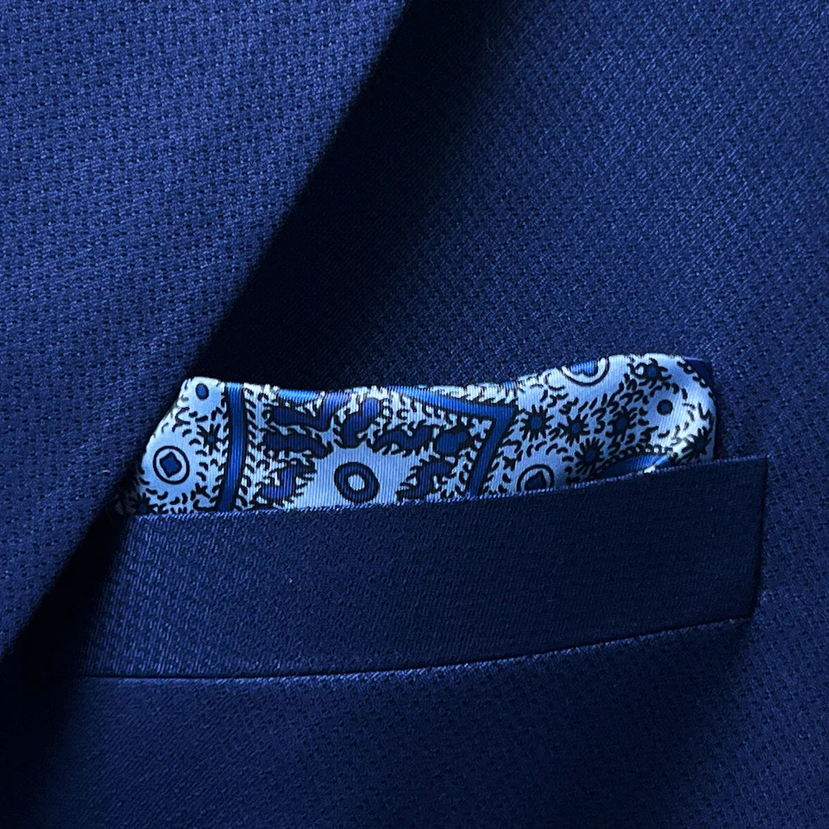 Breast pocket of navy blue geometric textured suit jacket with built-in pocket square holder and hand-finished edges