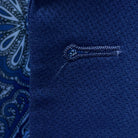 Detailed macro shot of hand-finished buttonhole stitching on navy blue geometric textured suit with light blue contrast thread