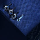 Suit jacket sleeve cuff showing functional buttonholes with contrast light blue accent stitching on navy blue geometric textured fabric