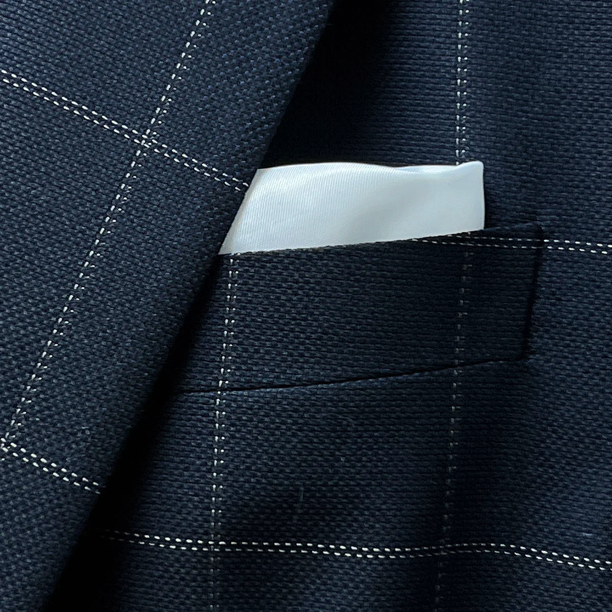 Close-up of white silk bemberg built-in pocket square in navy windowpane suit jacket breast pocket