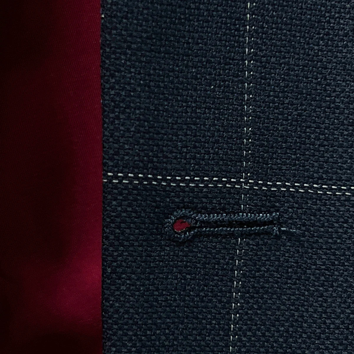 Macro view of buttonhole stitching on navy windowpane suit jacket, demonstrating quality craftsmanship