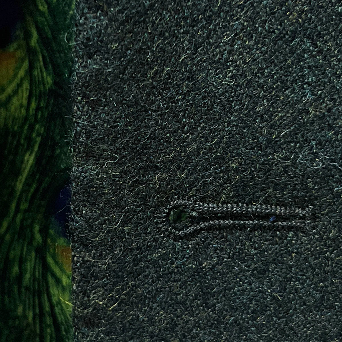 Detailed view of black contrast buttonhole stitching showing precise handwork on olive tweed fabric