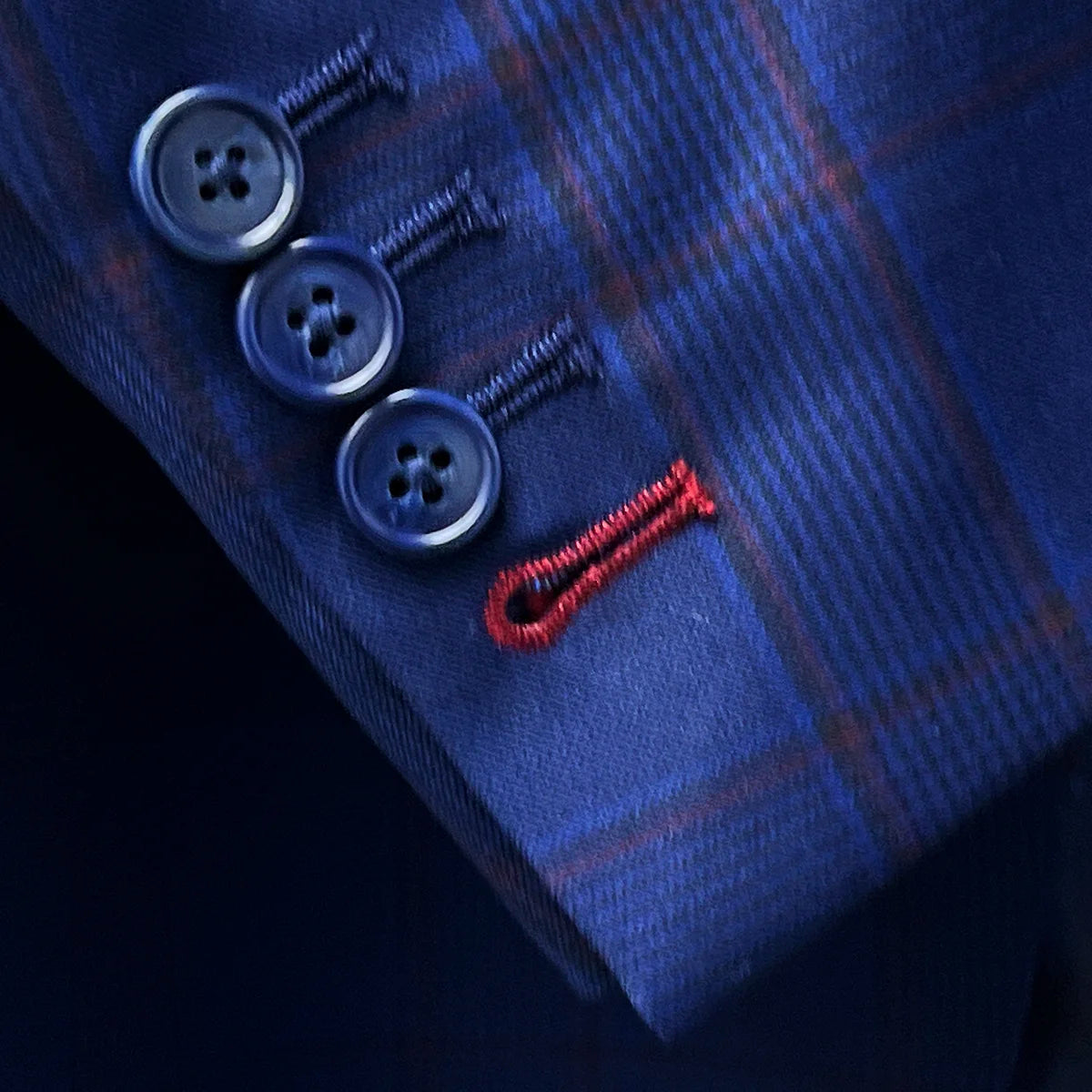 Close-up of functional sleeve buttonholes featuring crimson red contrast stitching detail on Super 140s merino wool fabric