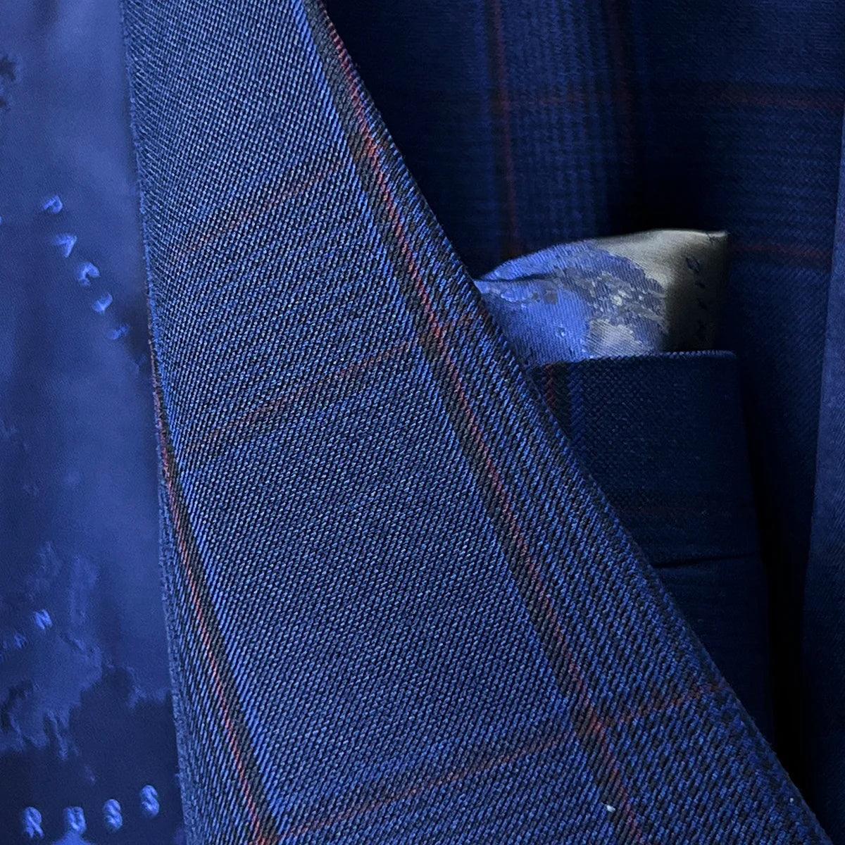 Lapel buttonhole detail with crimson red contrast stitching creating elegant accent against Prince of Wales plaid pattern
