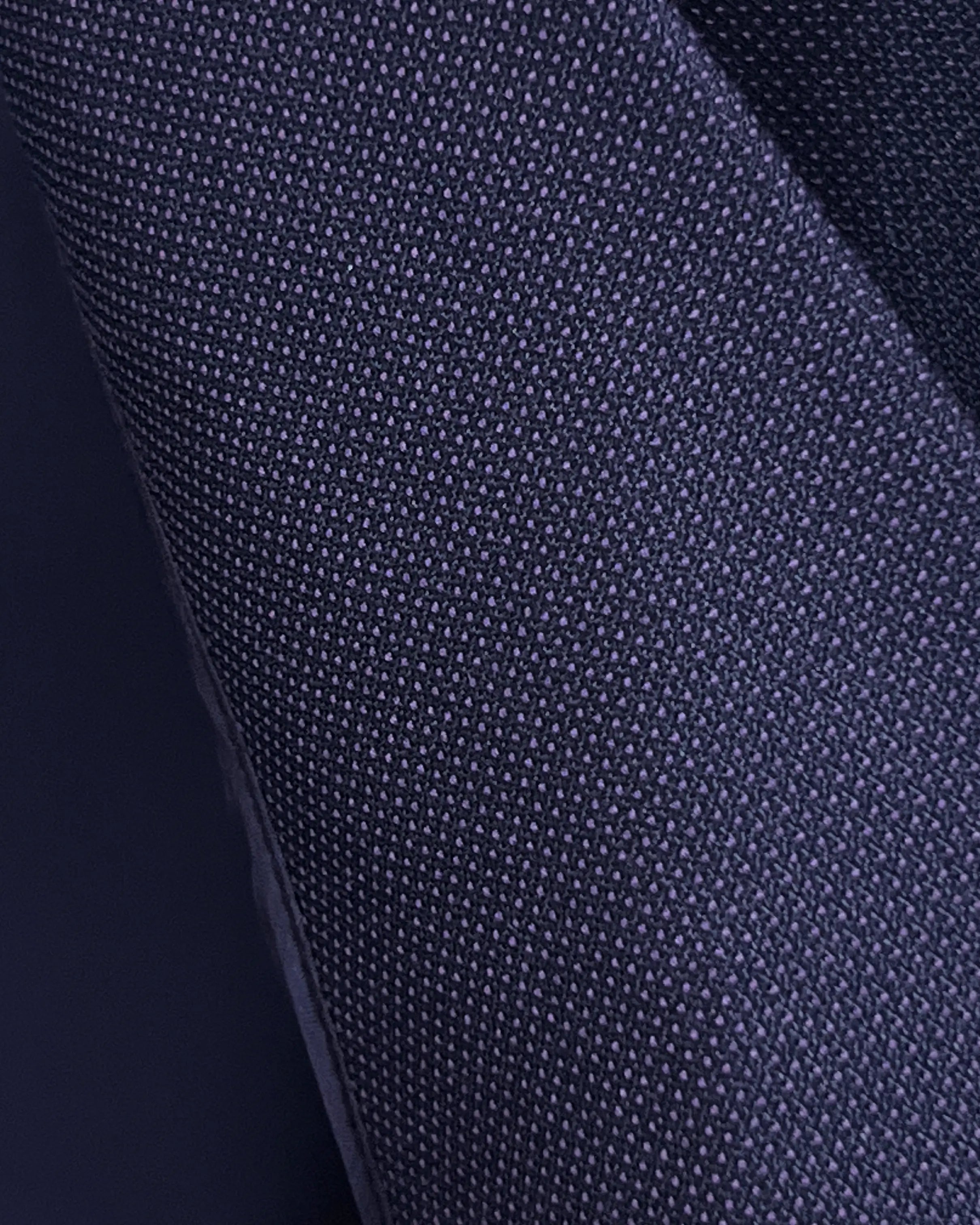 Fabric macro of aubergine birdseye men's suit showing fine birdseye weave and textured surface detail.