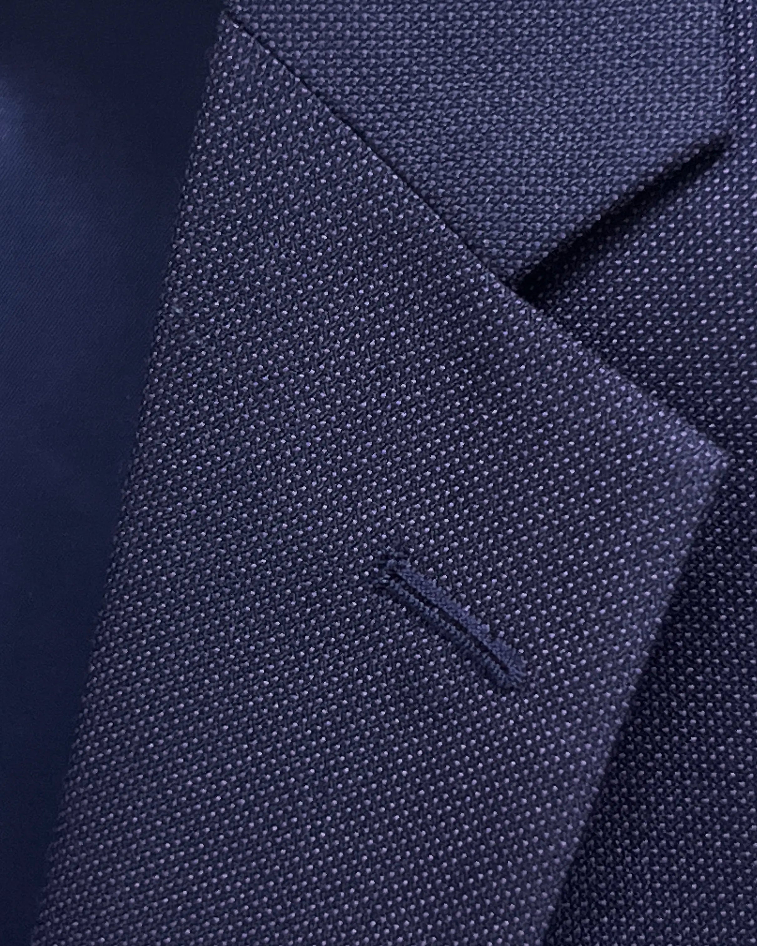 Lapel buttonhole close up of aubergine birdseye men's suit showing standard matching stitching.
