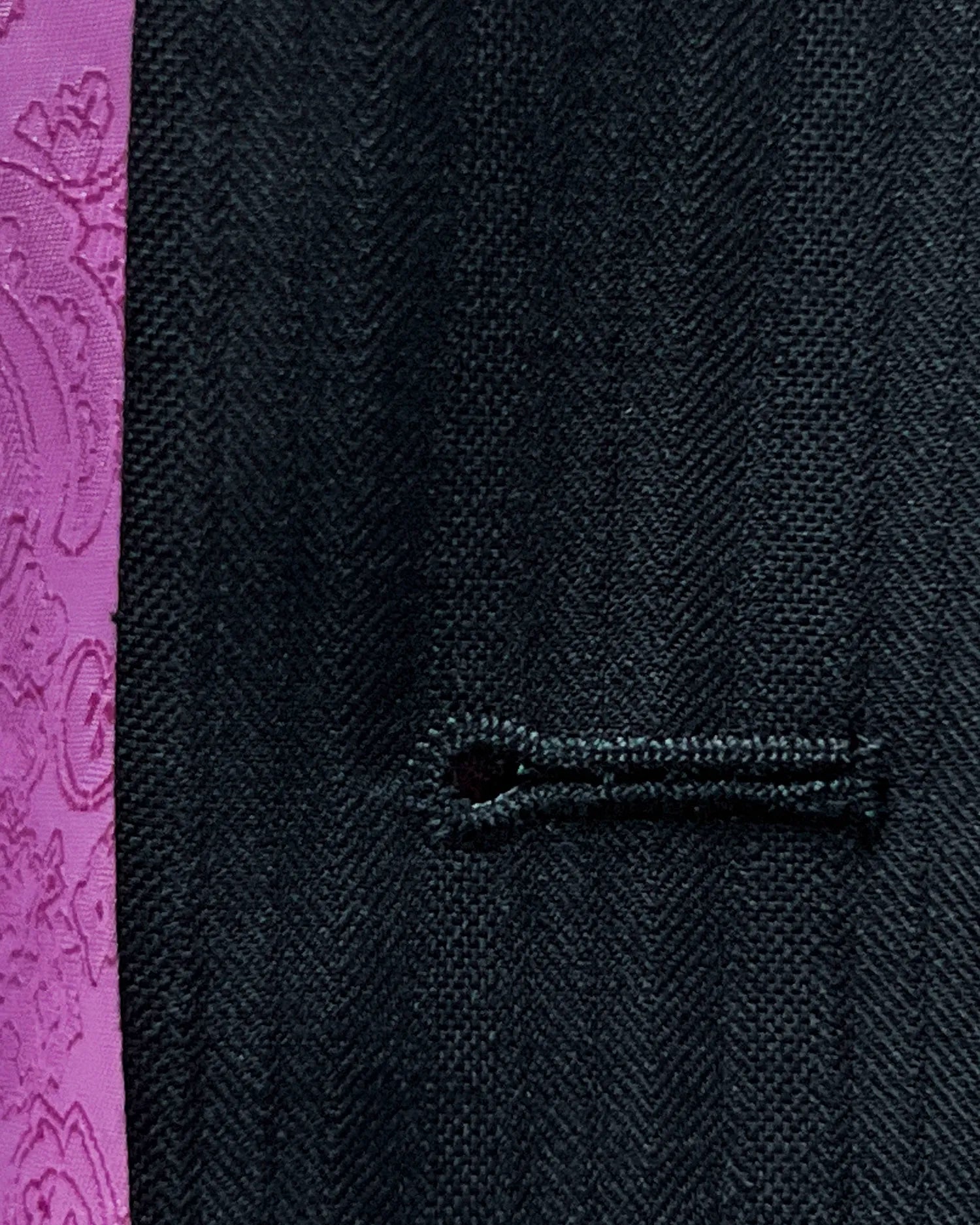 Buttonhole detail of black herringbone with shadow stripes men's suit showing the contrast light pink sleeve buttonhole
