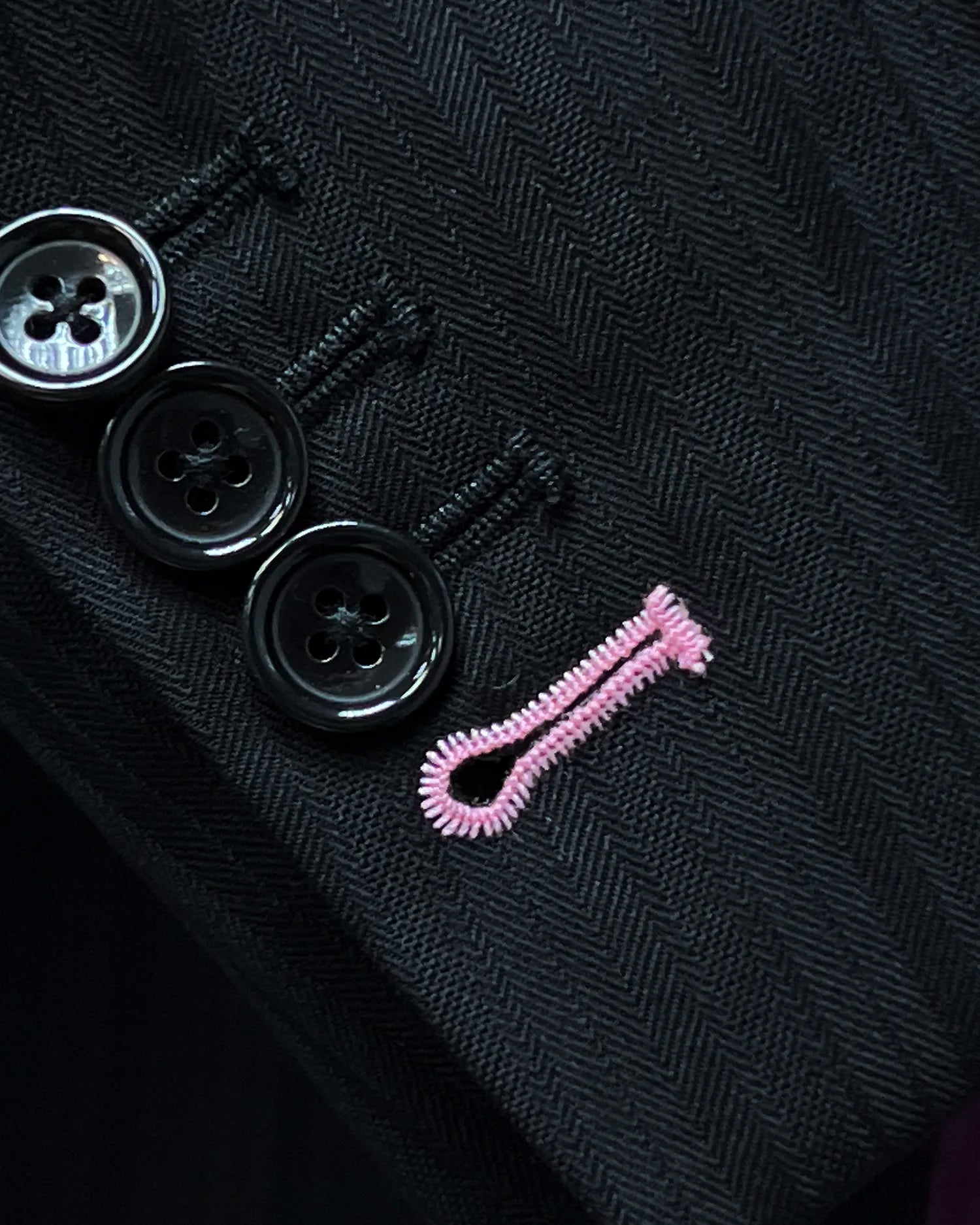 Sleeve detail of black herringbone with shadow stripes men's suit showing functional sleeve buttons and light pink final buttonhole