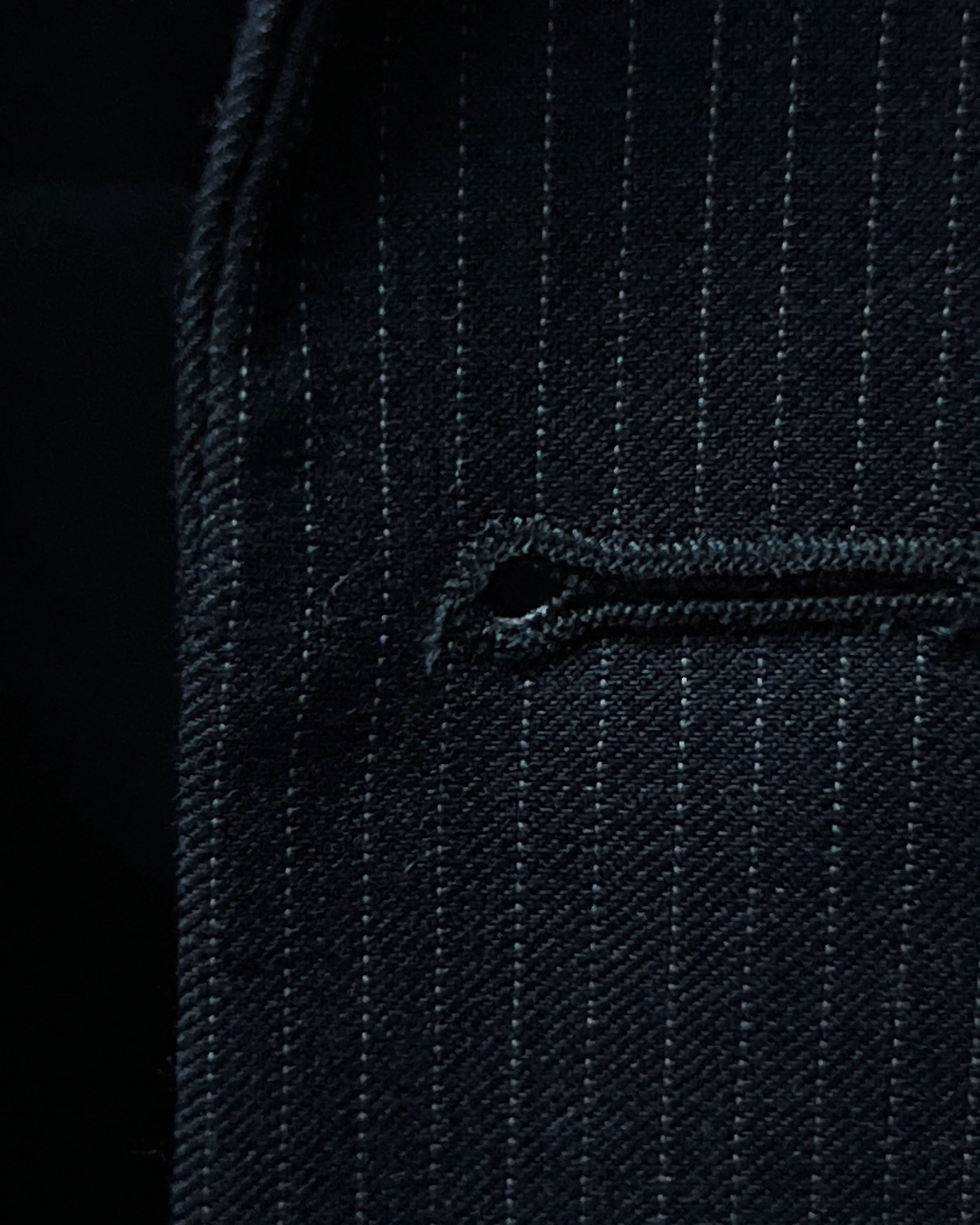 Front buttonhole detail of black pinstripe men's suit showing clean standard stitching and tailored construction