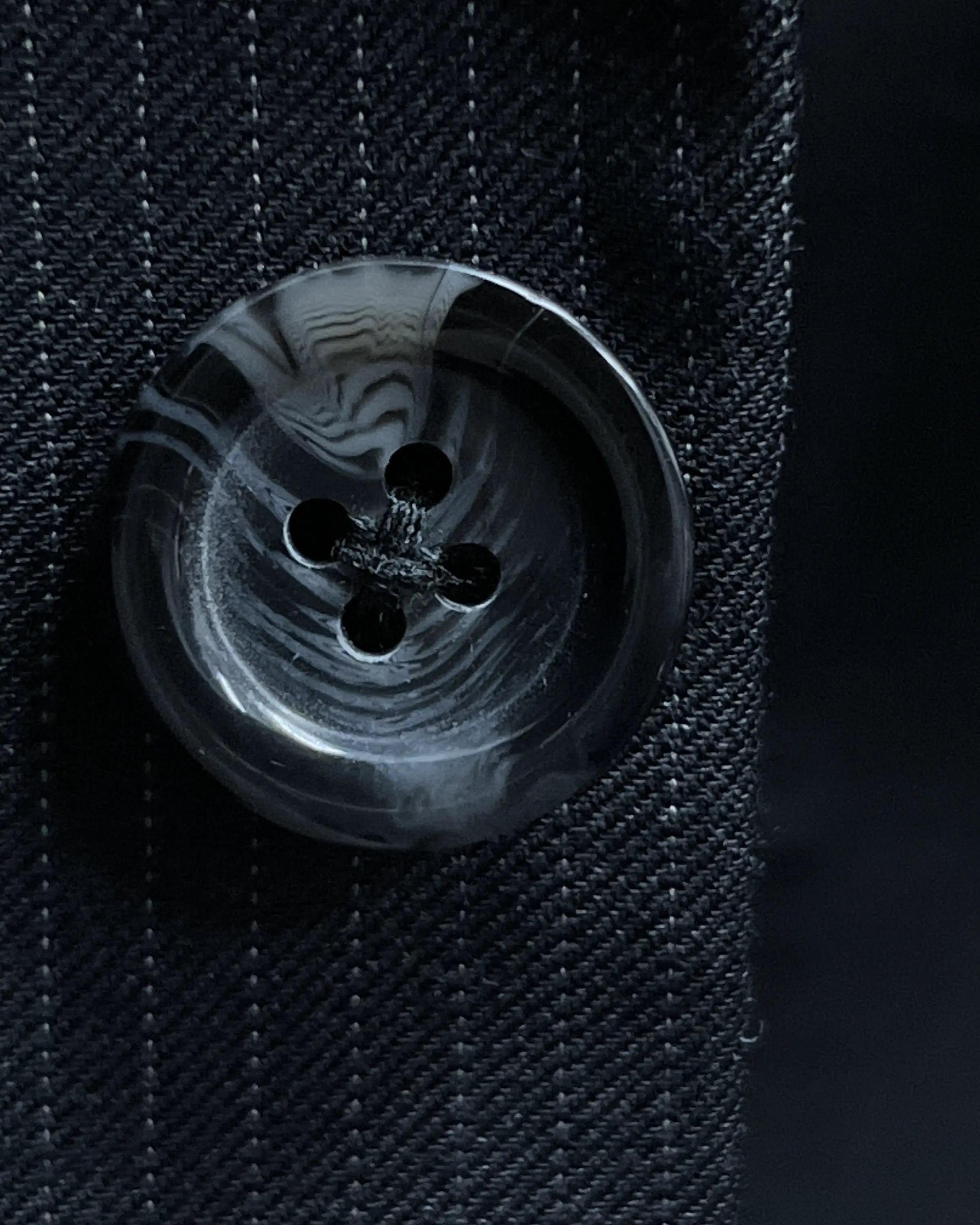 Dark charcoal marble horn buttons on black pinstripe men's suit showing polished natural button surface and tailored stitching