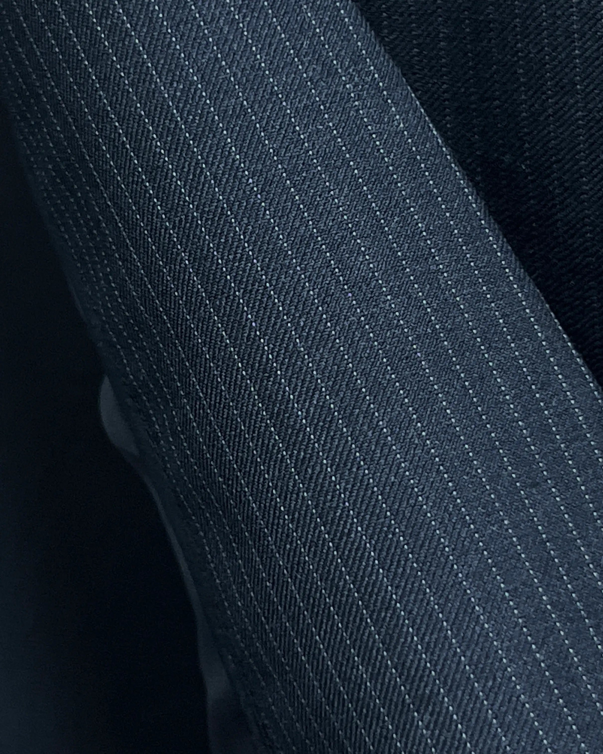 Fabric cloth texture of black pinstripe men's suit showing fine woven stripe structure and suiting surface