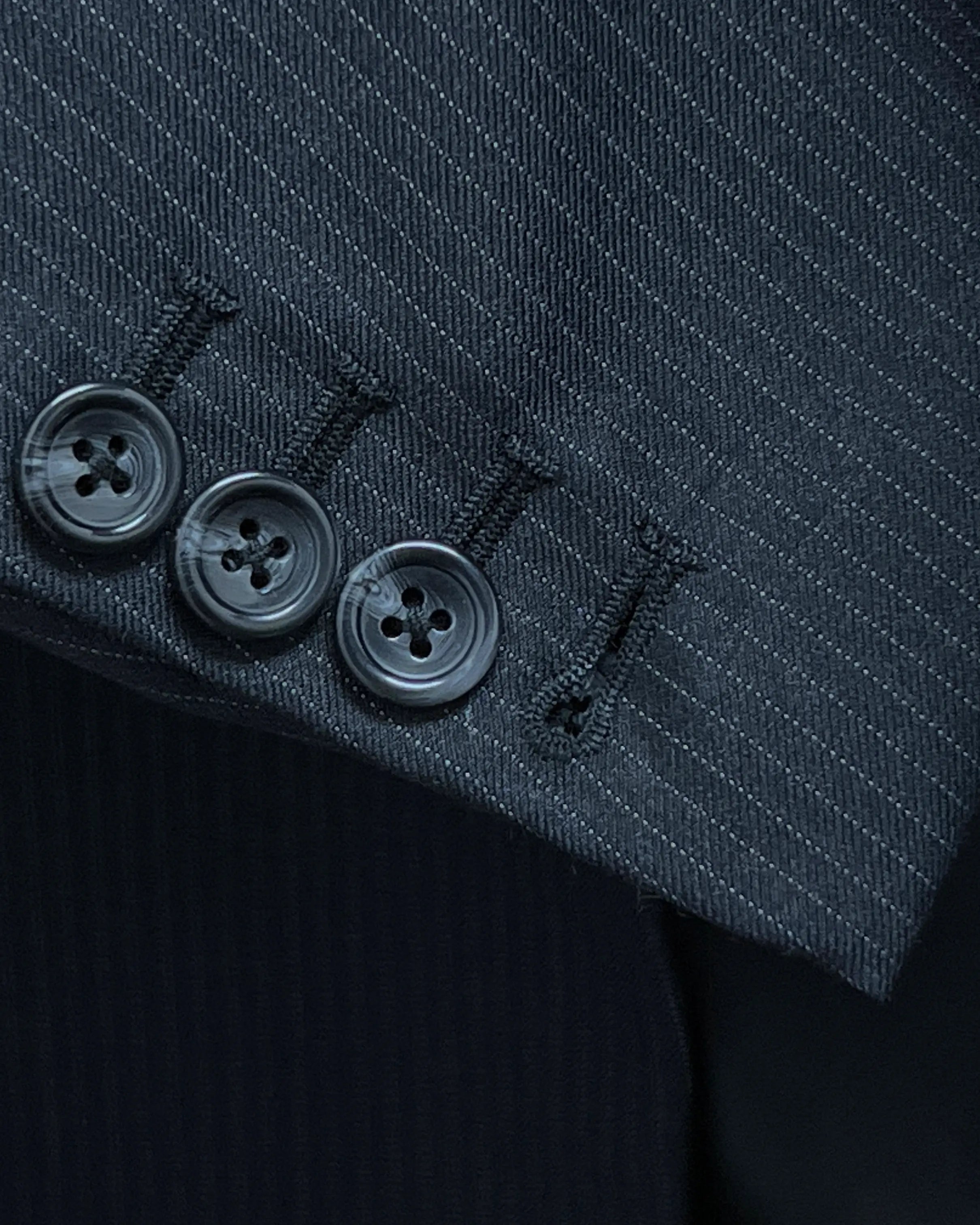 Functional sleeve button detail of black pinstripe men's suit showing standard matching buttonhole stitching