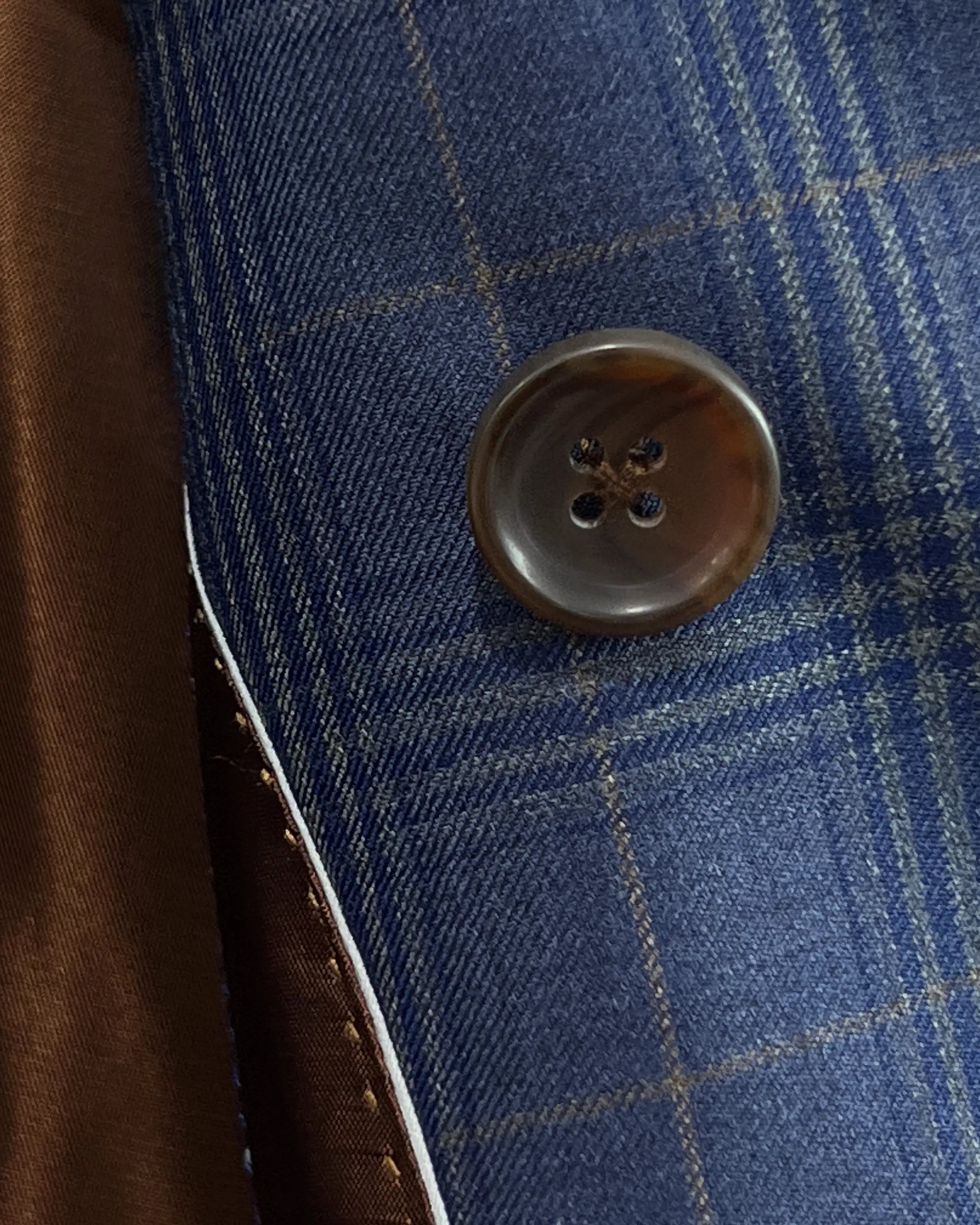 Button detail of blue windowpane plaid men's suit showing medium brown horn buttons