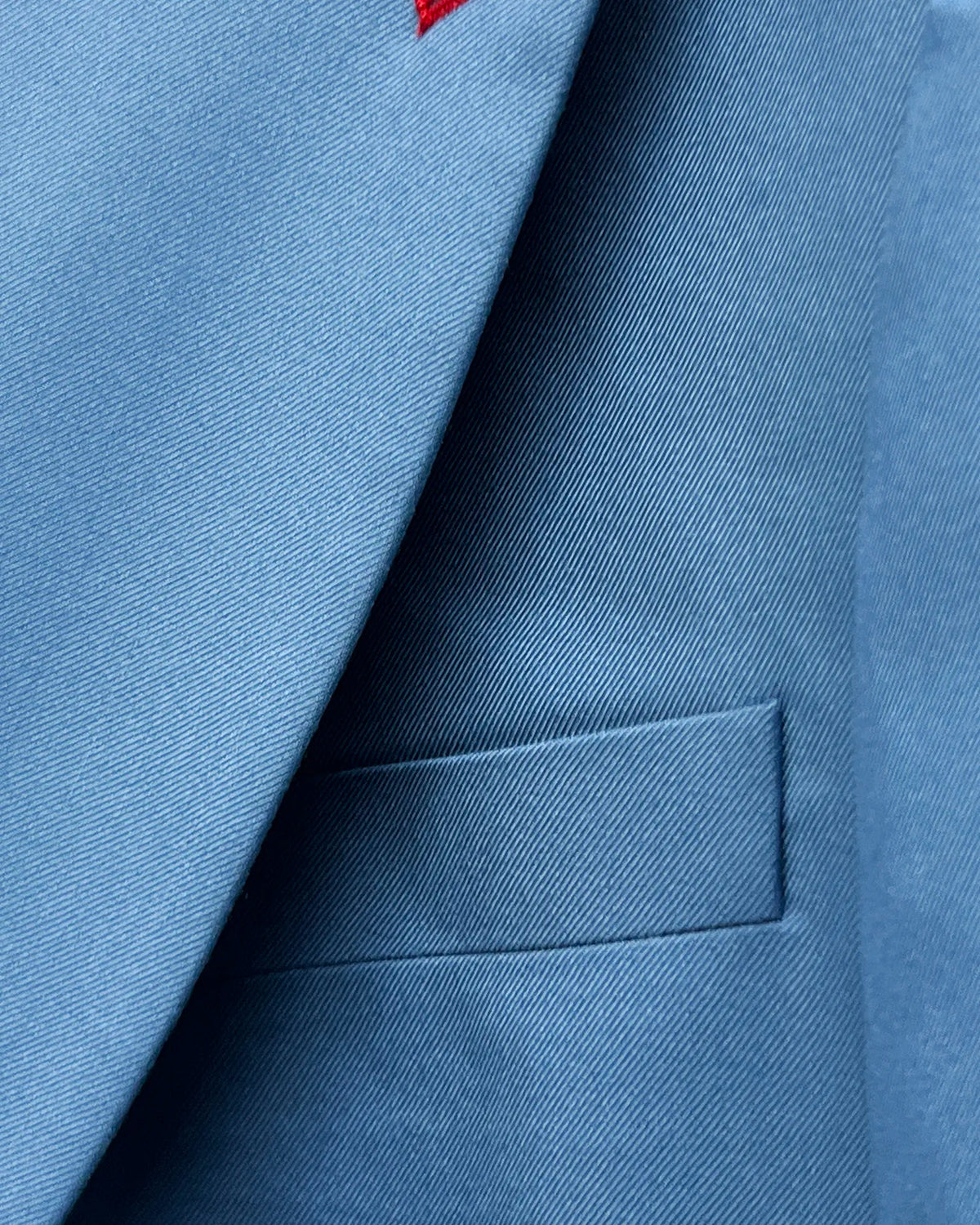 Chest detail of cornflower blue solid twill weave men's suit showing white built in lining pocket square