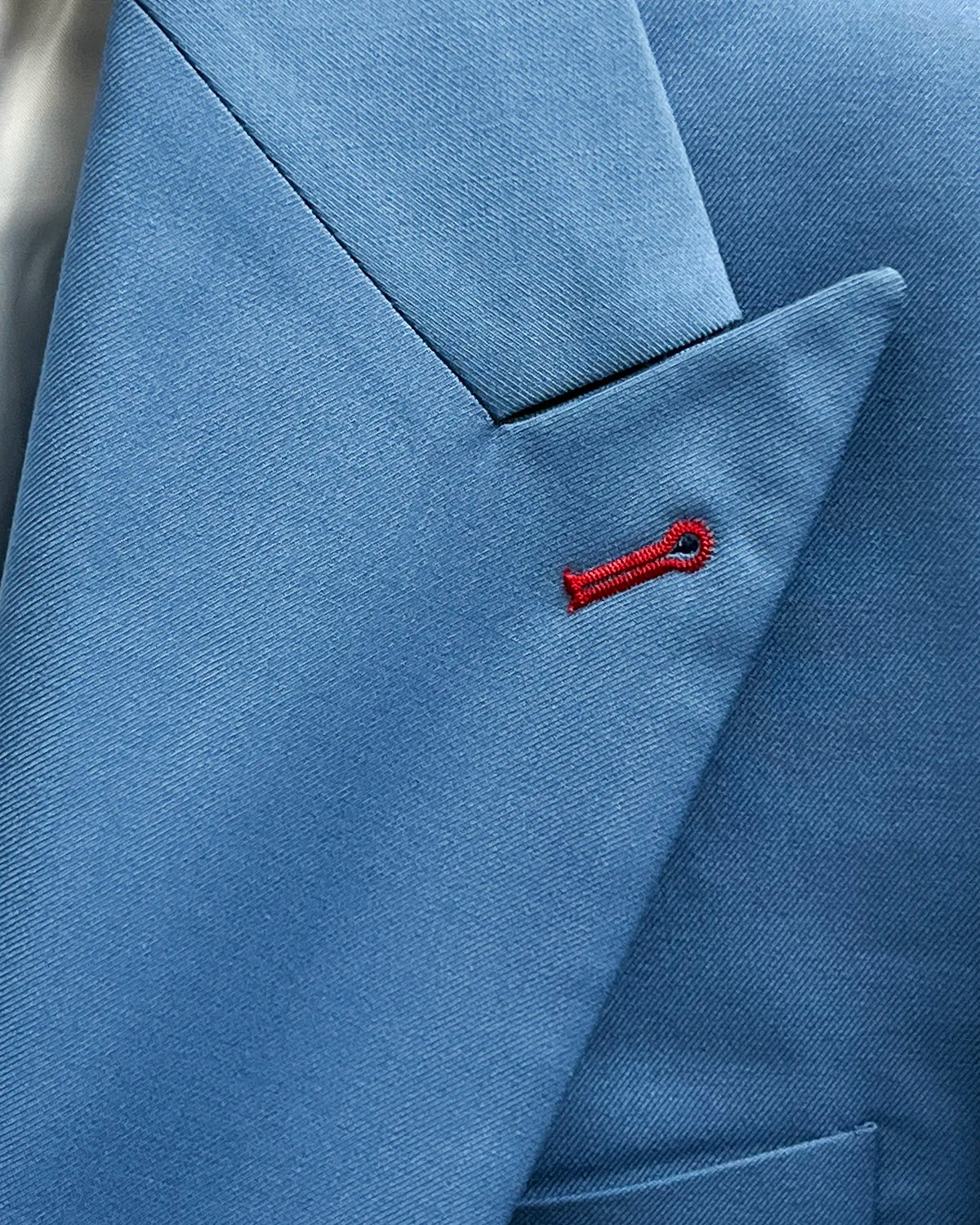 Peak lapel detail of cornflower blue solid twill weave men's suit showing burgundy contrast lapel buttonhole