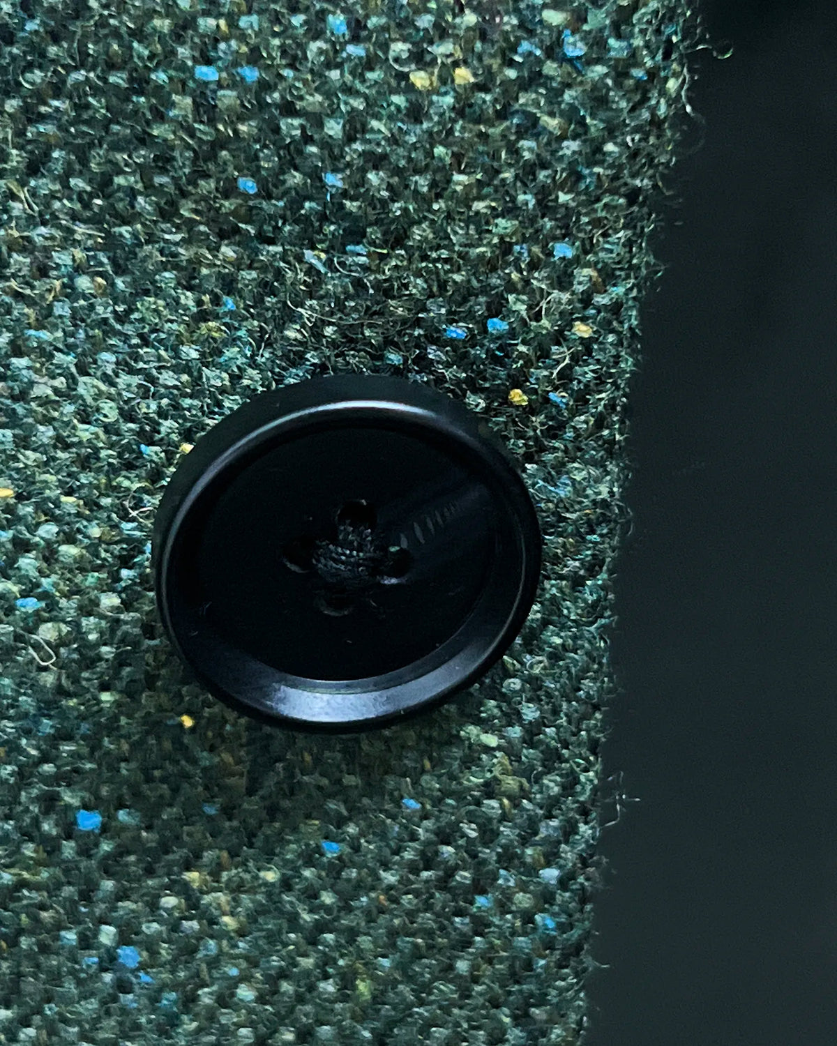 Button detail of dark forest green Donegal tweed men's suit showing black horn buttons