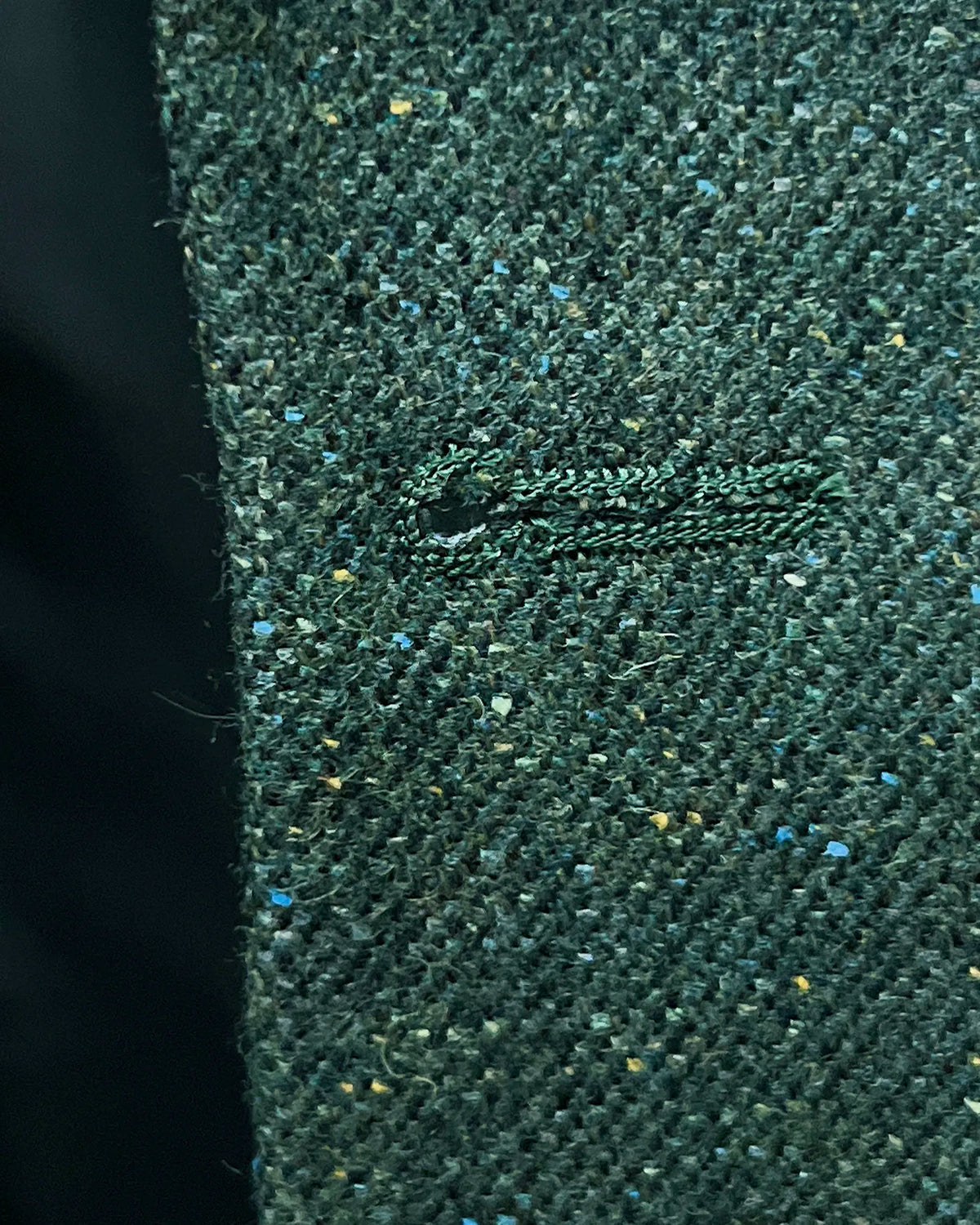 Buttonhole detail of dark forest green Donegal tweed men's suit showing clean matching stitching