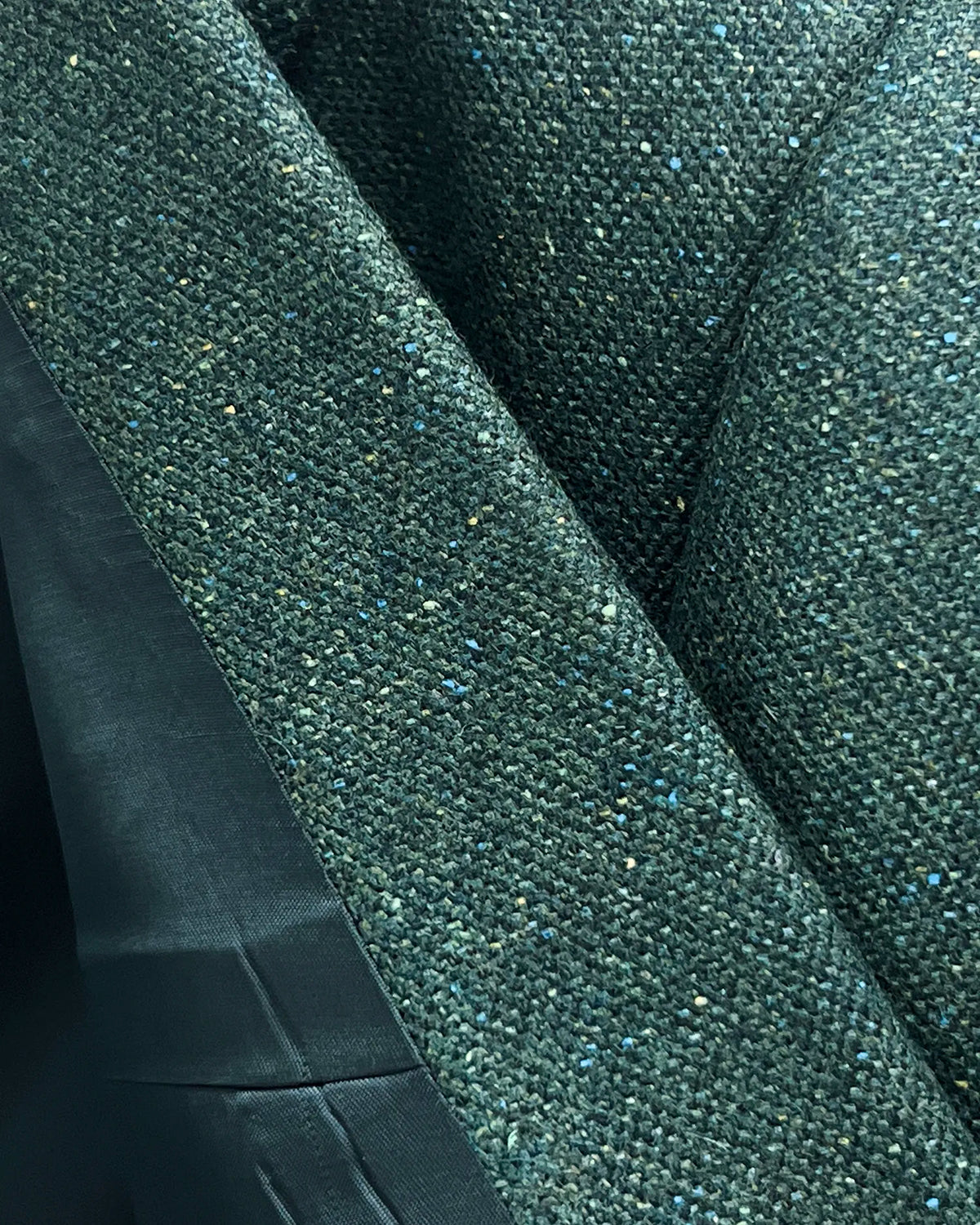Fabric close up of dark forest green Donegal tweed men's suit showing the textured wool silk cloth and flecked surface