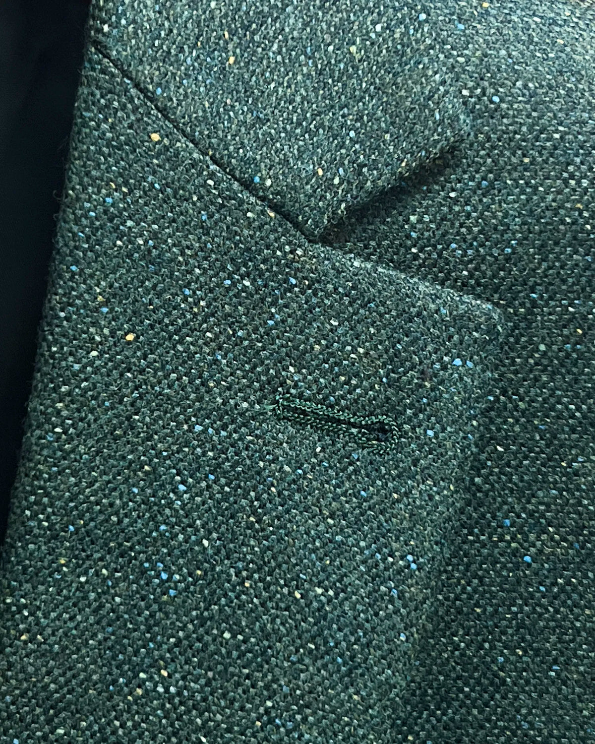 Lapel detail of dark forest green Donegal tweed men's suit showing the standard matching lapel buttonhole