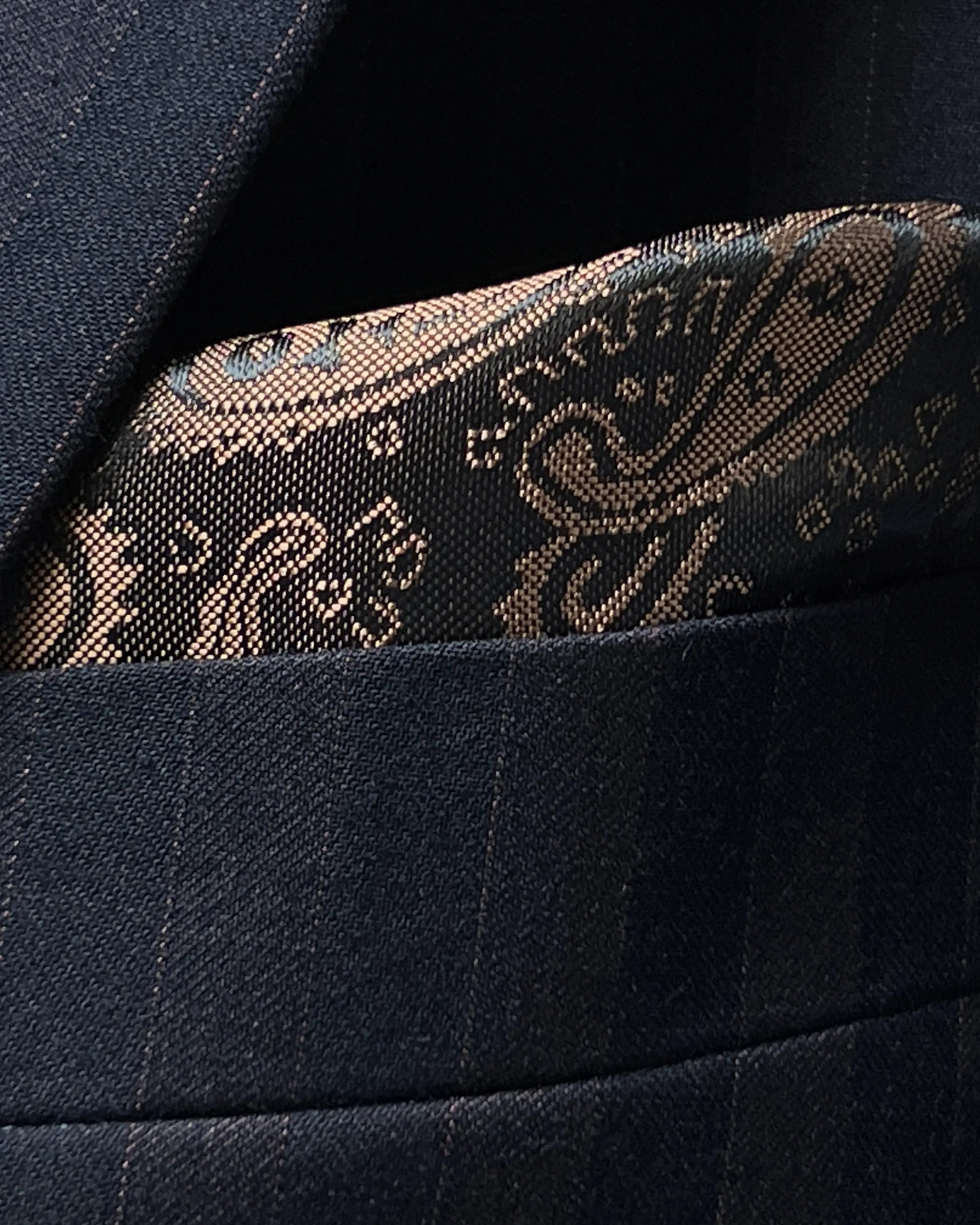 Pocket square detail of dark navy with brown herringbone stripe men's suit showing lining matched pocket square.