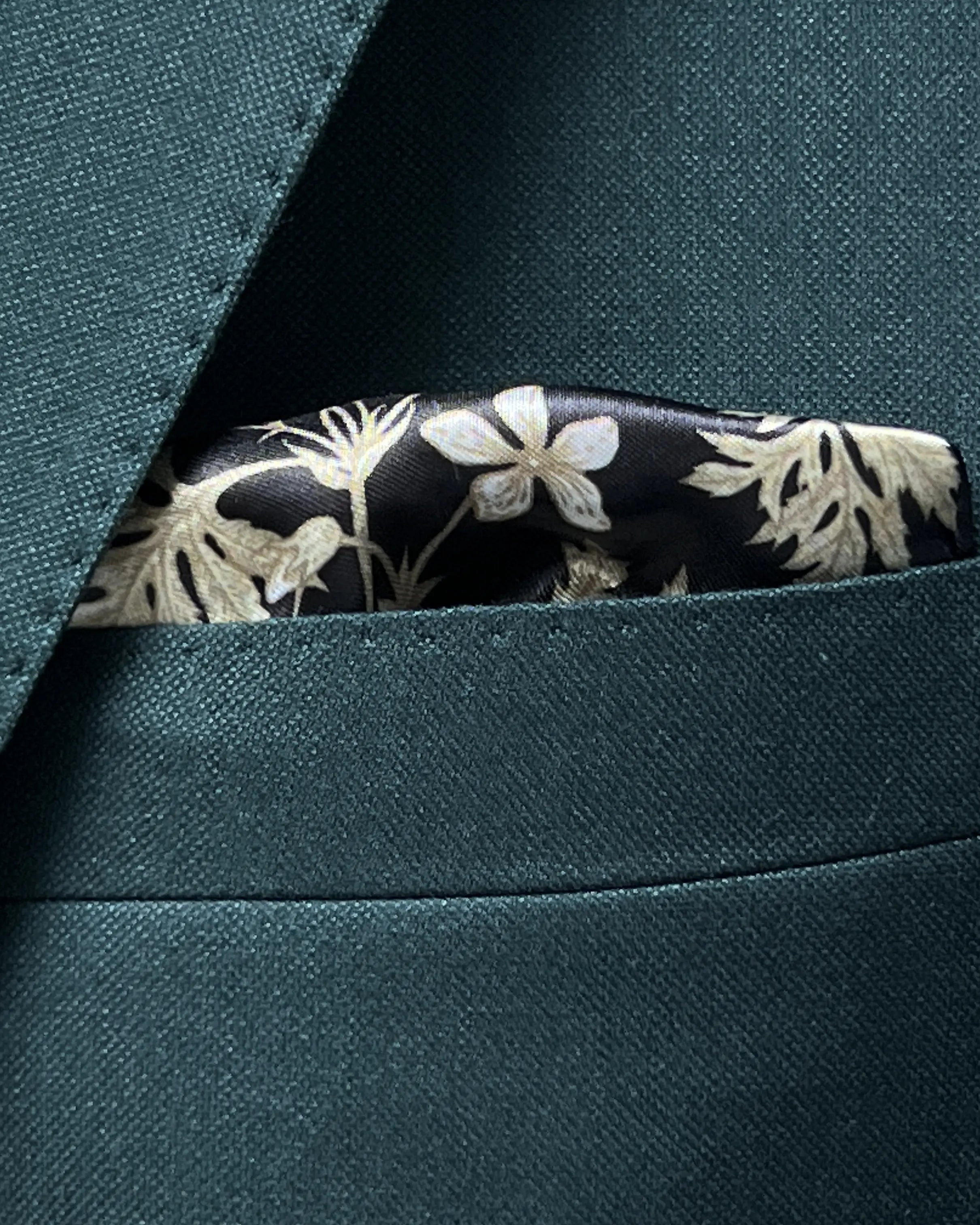 Built in lining pocket square detail of deep teal green solid men's suit showing matching black floral lining fabric