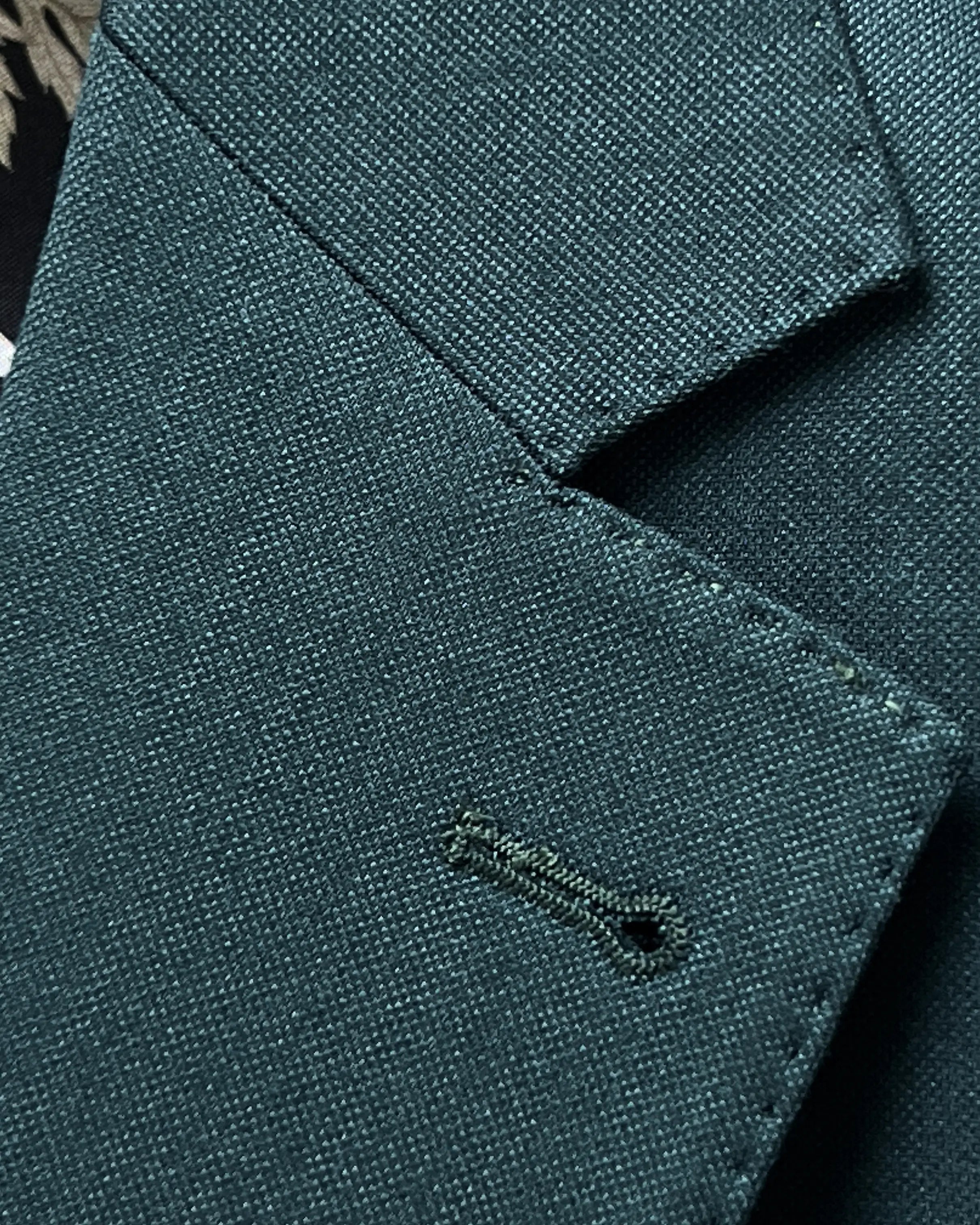Lapel buttonhole detail of deep teal green solid men's suit showing matching Milanese buttonhole stitching