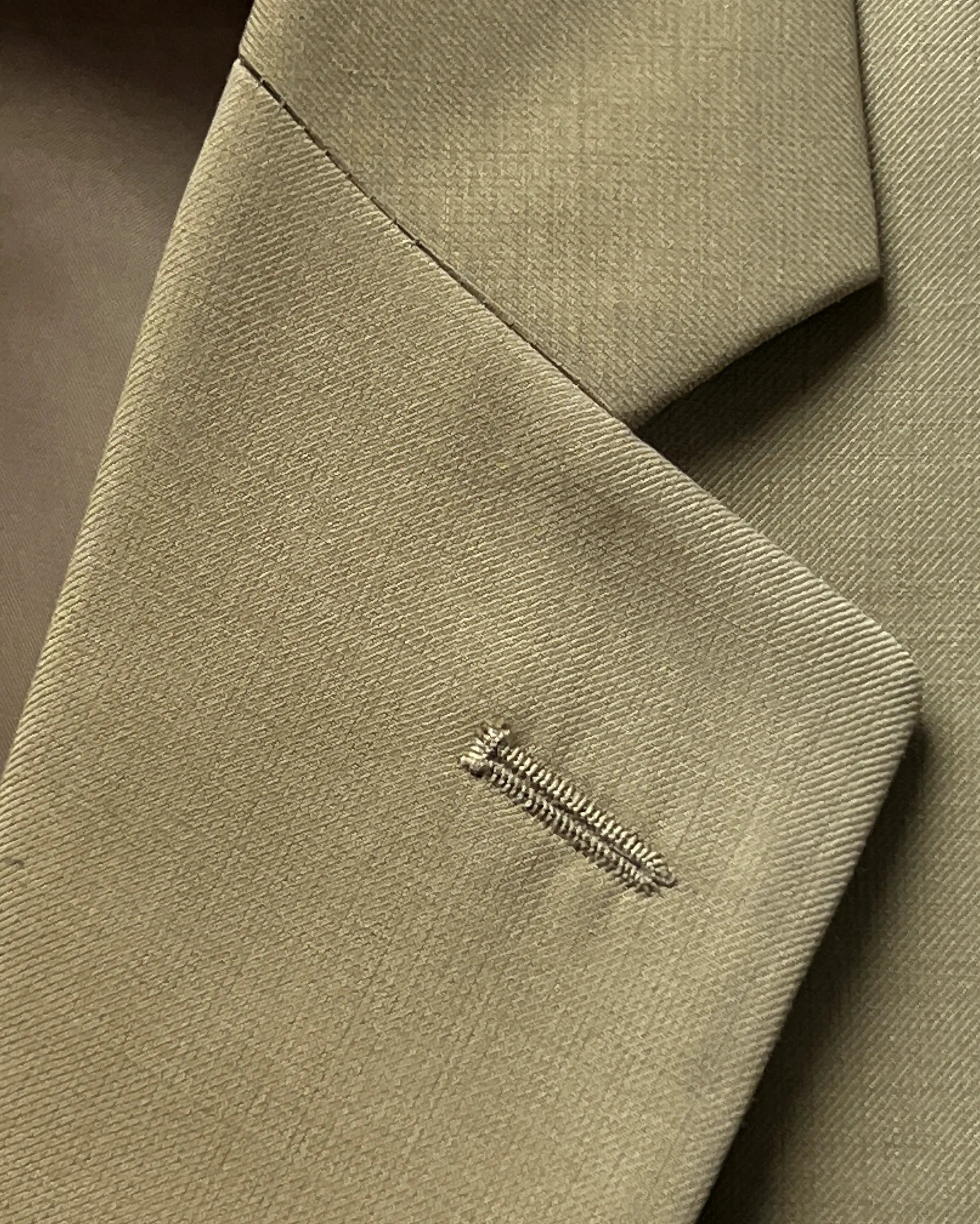Lapel close up of brown plain men's suit showing matching lapel buttonhole detail