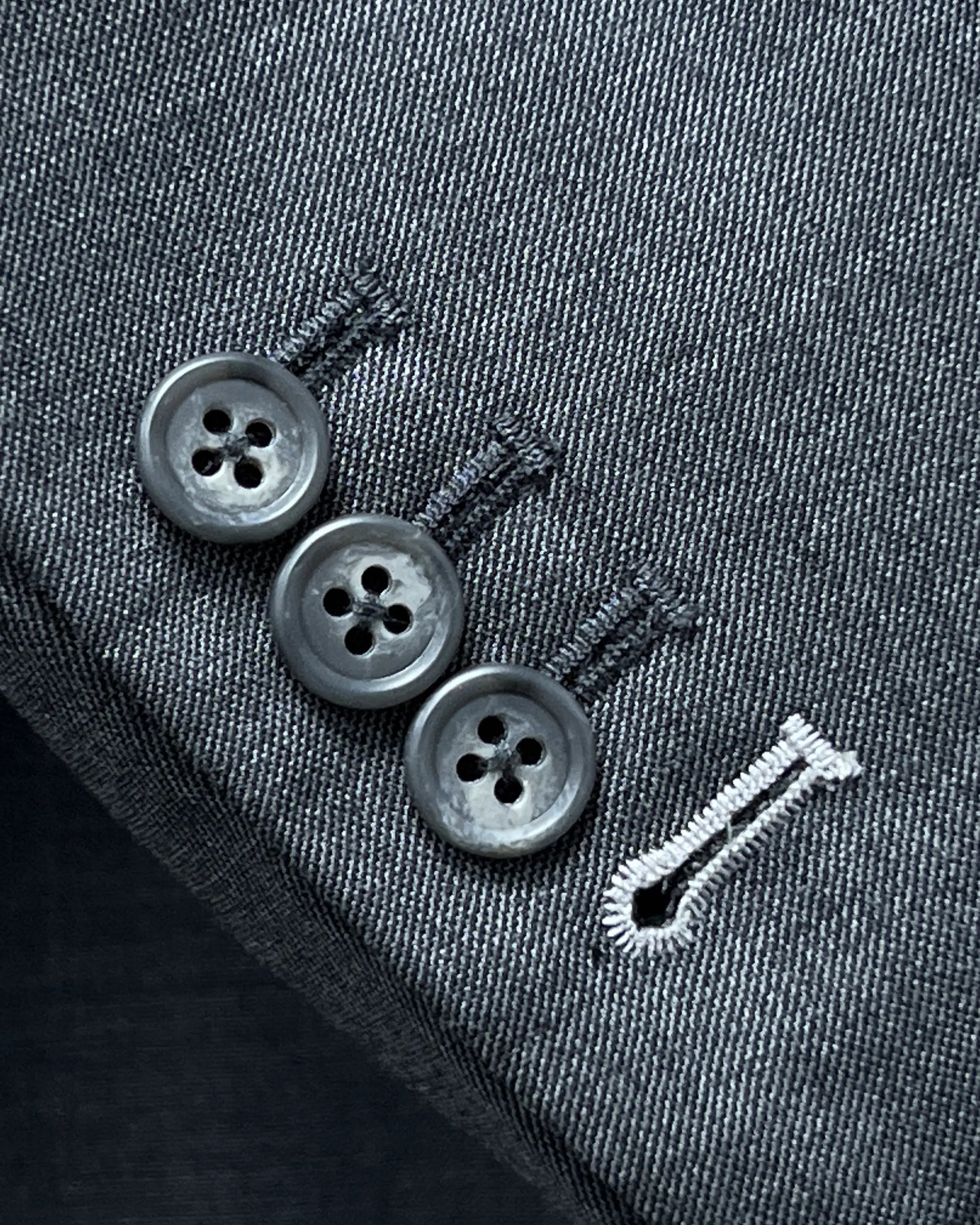 Functional sleeve button close up of medium grey sharkskin men's suit showing surgeon cuffs and white contrast last sleeve buttonhole