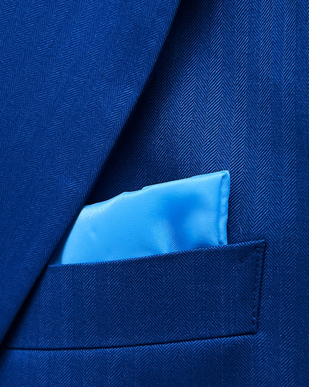 Chest detail of royal blue herringbone men's suit showing matching sky blue lining pocket square