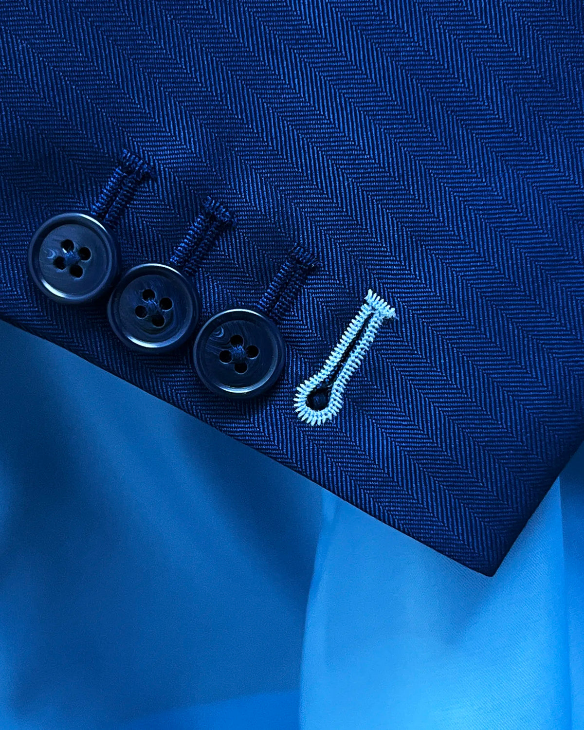 Sleeve detail of royal blue herringbone men's suit showing functional buttons and ivory contrast last buttonhole