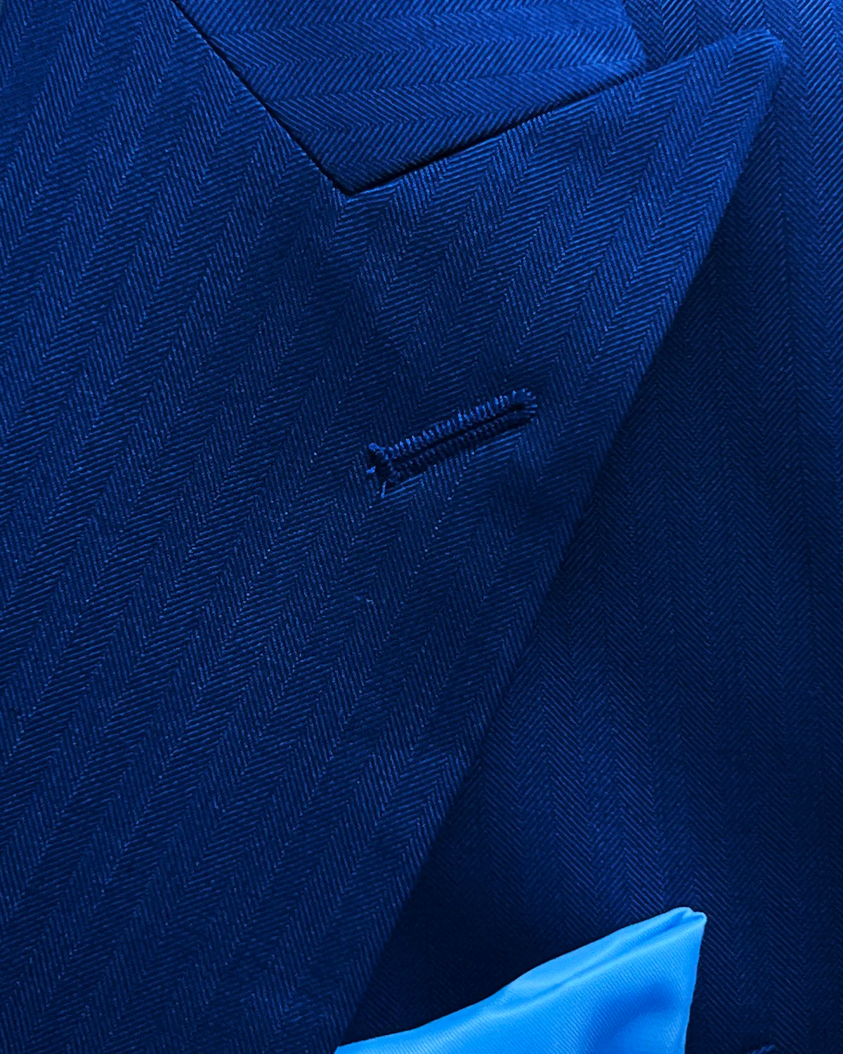 Lapel detail of royal blue herringbone men's suit showing standard peak lapel buttonhole