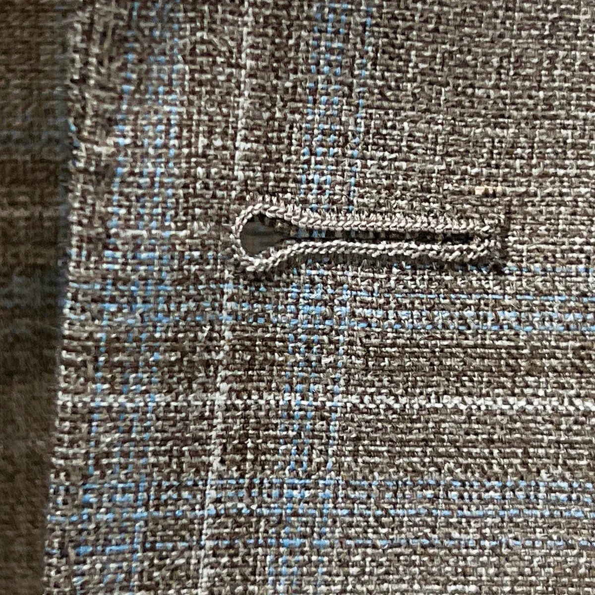 Detailed macro shot of hand-finished buttonhole stitching on tan blue windowpane sport coat with sky blue contrast thread