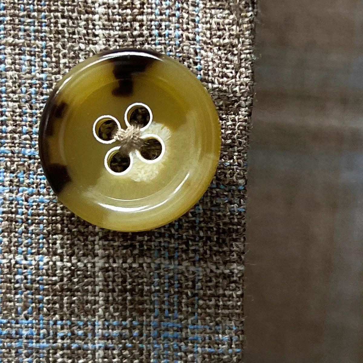 Close-up of tan and deep brown horn buttons on tan blue windowpane sport coat showing natural marble-like patterns